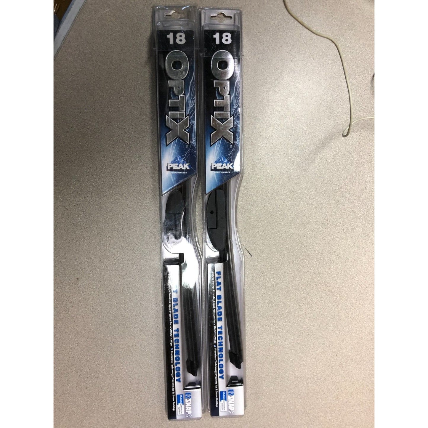 Two packages of Optix Peak windshield wiper blades on a beige surface.