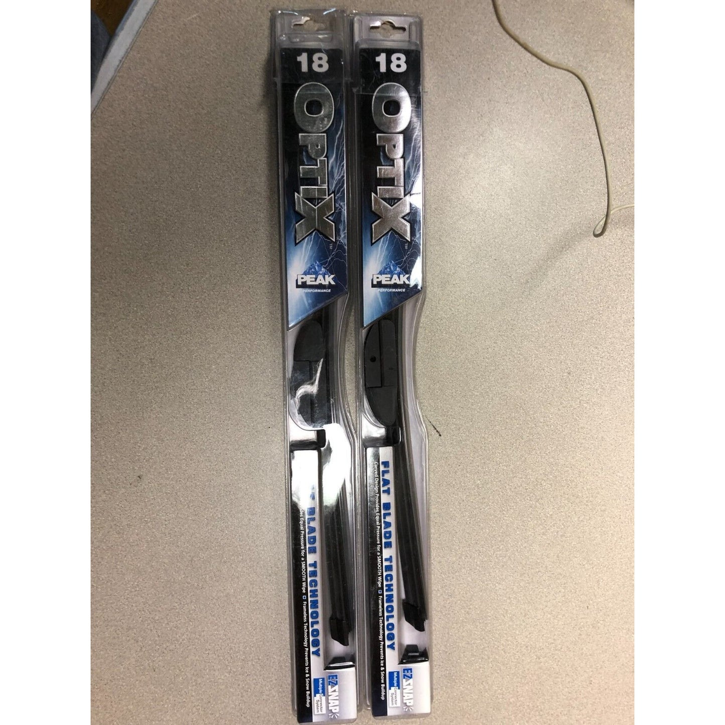 Two packages of Optix peak wiper blades on a beige surface