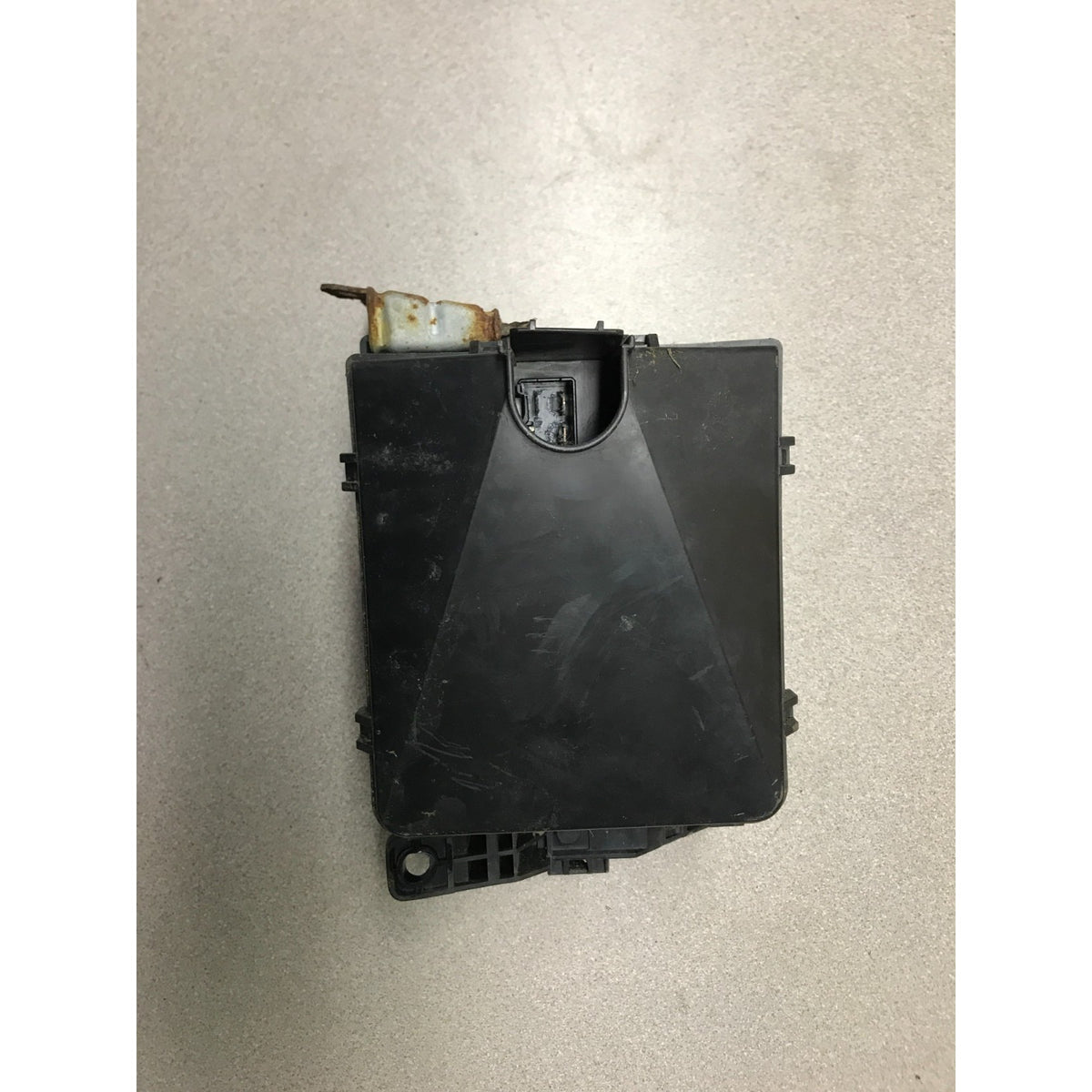 A black plastic automotive electronic control module with a small rusty metal tab protruding from the top, photographed on a light gray floor. 1993 Honda Civic Del Sol OEM Engine Bay Fuse Box back view
