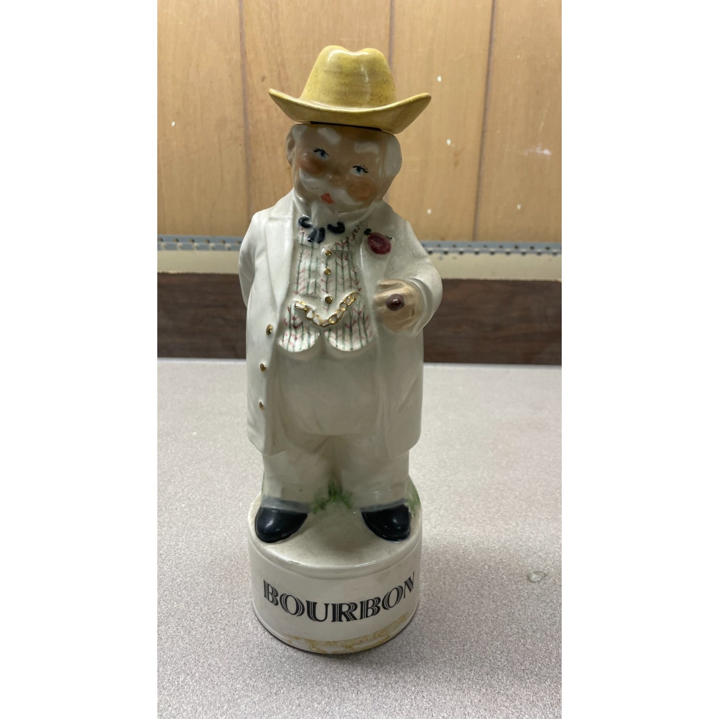 Decorative figurine of a man in a white coat and yellow hat with 'Bourbon' branding on a plain background.