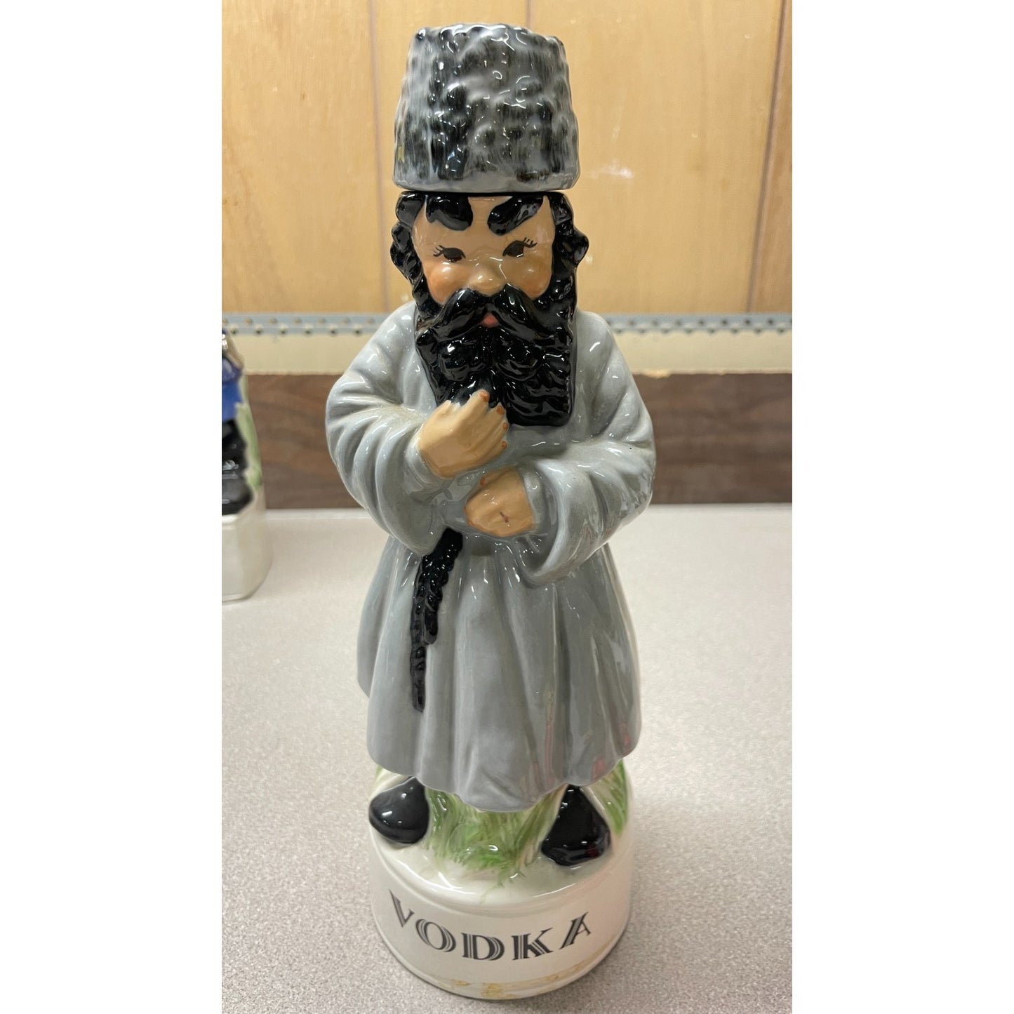 Statue of a man in traditional attire on a vodka bottle with a wooden background