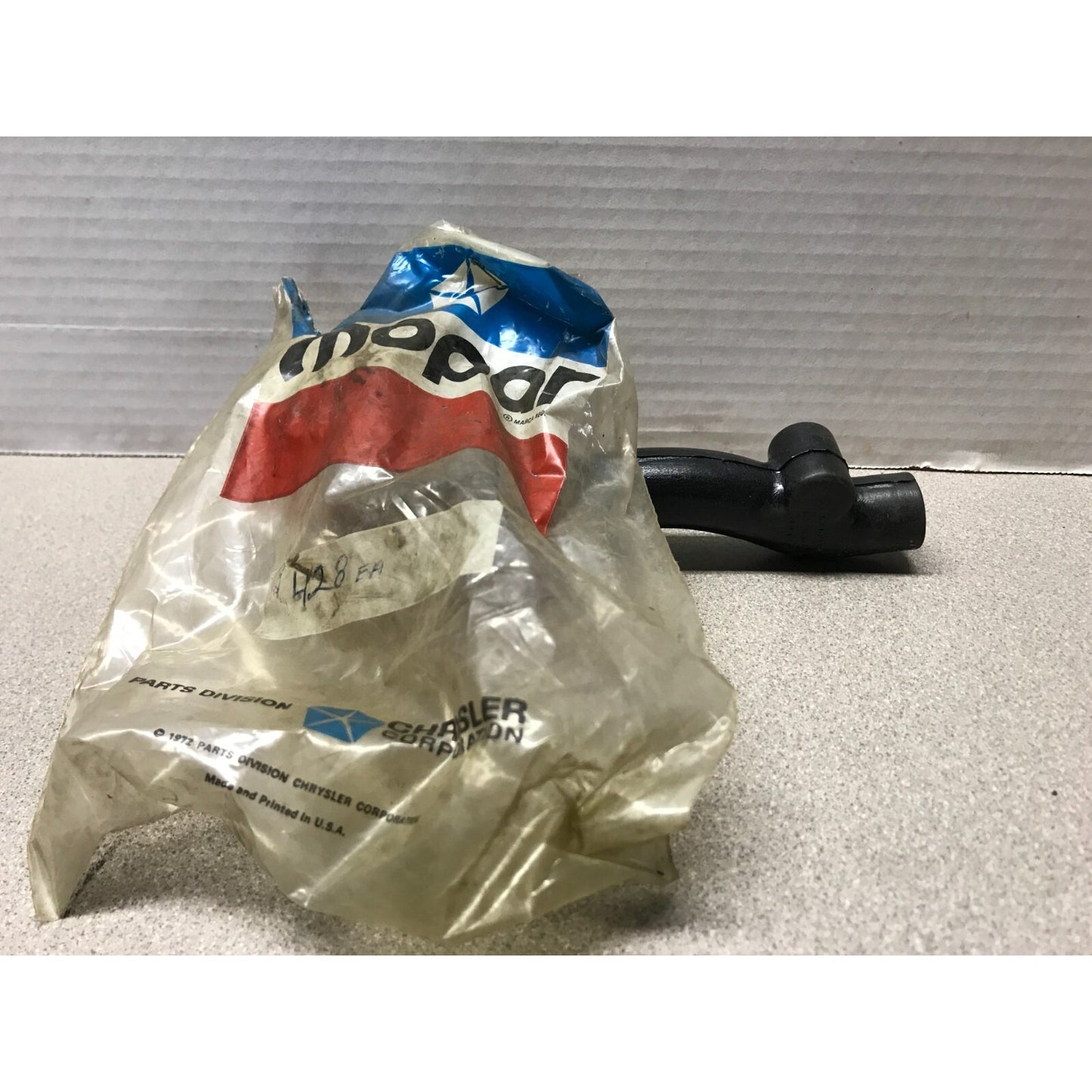 Black motorcycle part on a gray surface with a partially open Mopar bag.
