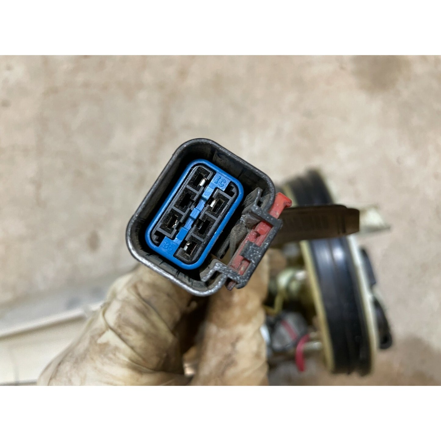 Car ignition switch connector held by a gloved hand against a blurred background