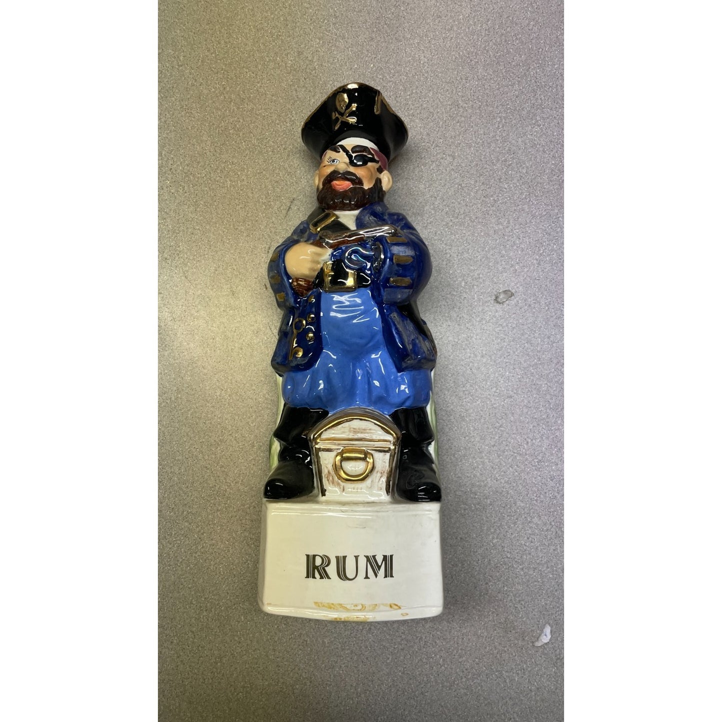 Figurine of a person in blue uniform holding a bottle labeled 'Rum' on a gray background