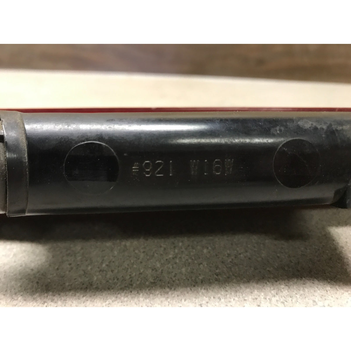 Close-up of a black metal cylindrical component with stamped markings reading “#921 W16W” on a neutral surface. 2005-2010 Honda Odyssey OEM High Mount Third Brake Light