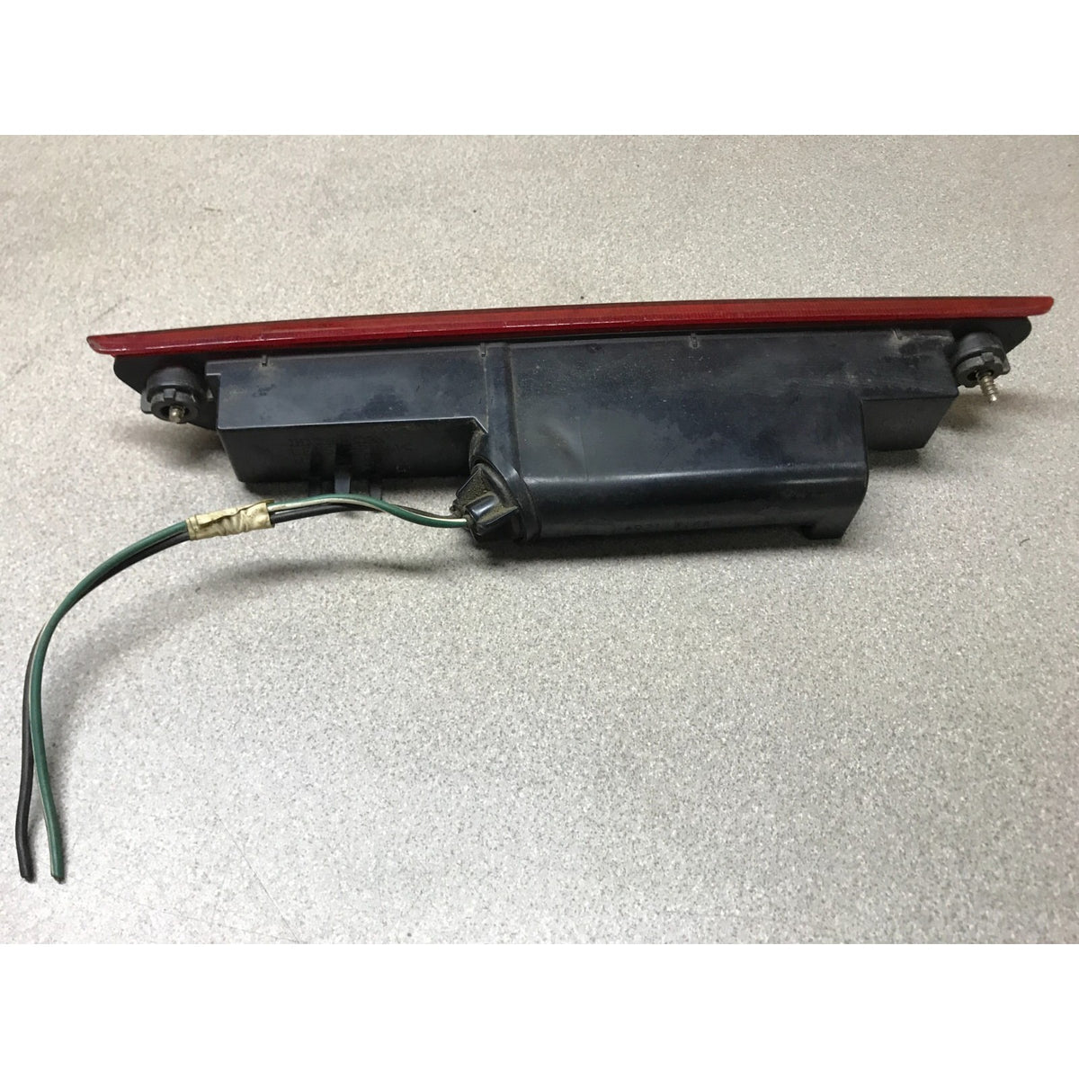 A used automotive light assembly, brake light, featuring a black plastic housing, a red lens, and a green wire harness, photographed on a gray textured surface. 2005-2010 Honda Odyssey OEM High Mount Third Brake Light