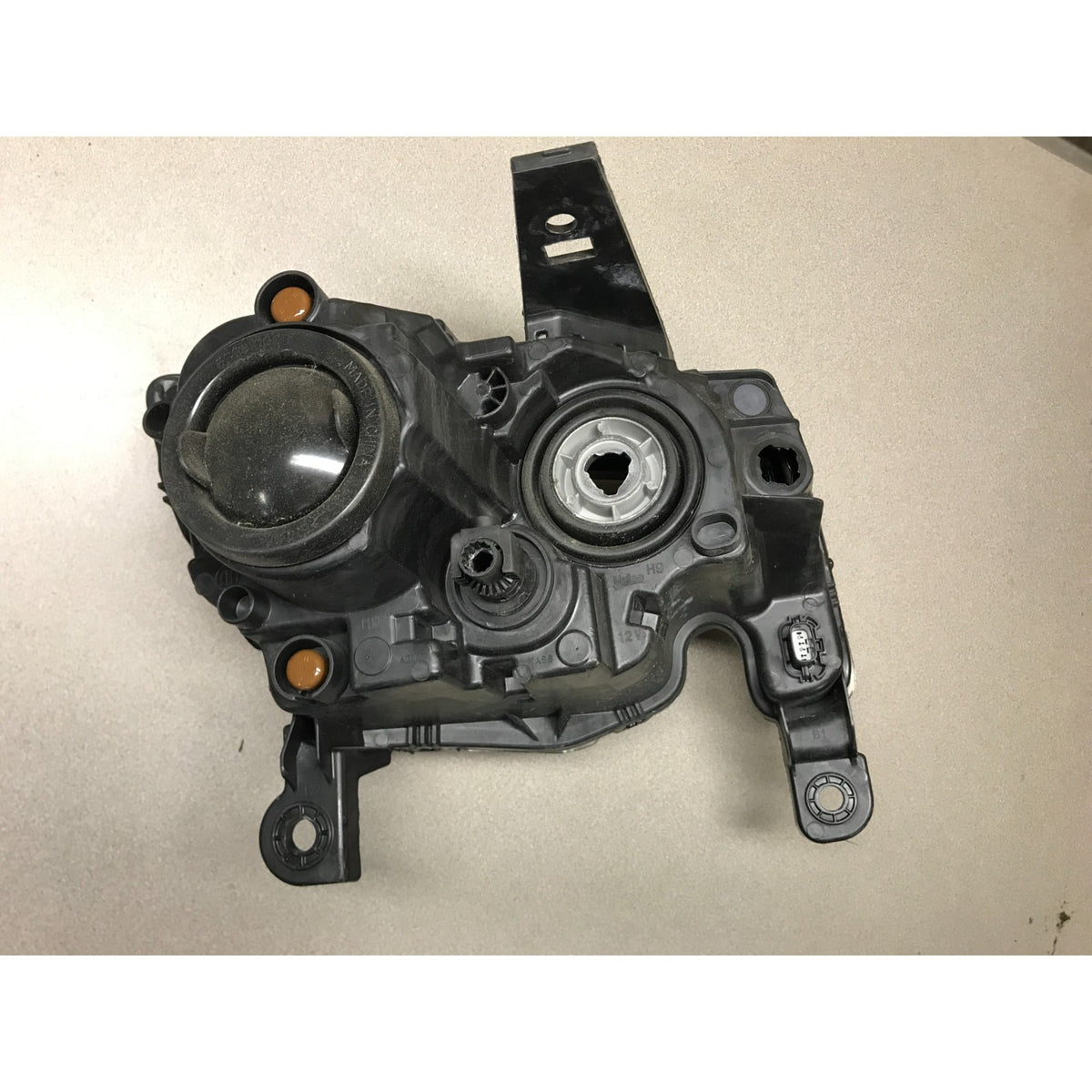A black plastic automotive part with molded housing, mounting tabs, and circular openings, photographed on a light beige surface. 2019 Jeep Grand Cherokee Altitude Front Left LH Drivers Side OEM Headlight Lens