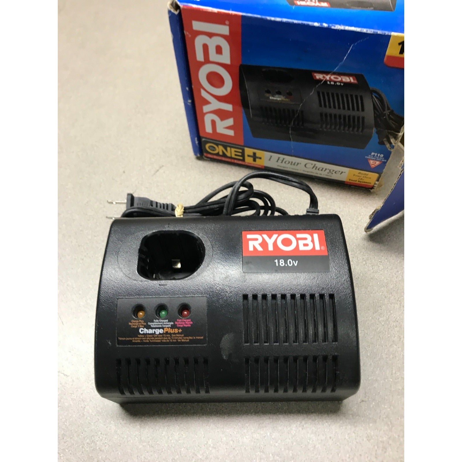 Ryobi battery charger with power cord on a light gray surface, box in the background.