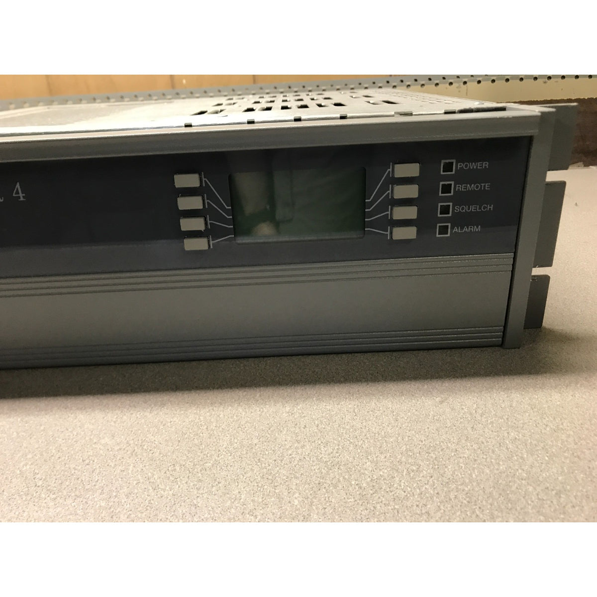 A gray industrial electronic control panel or rack-mounted device with a small display window and labeled buttons for POWER, REMOTE, COUBLON, and ALARM, photographed on a carpeted floor. MRC Coderunner 4 Central Receiver closeup of right front panel controls