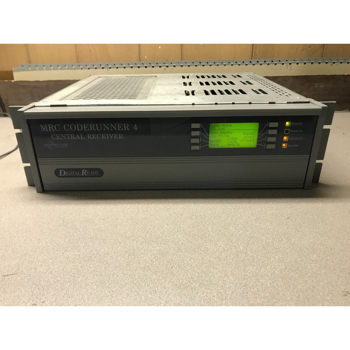 Digital-Radio MRC Coderunner 4 Central Receiver device in a gray rack-mount enclosure, with a small green display screen and indicator lights on the front panel. MRC Coderunner 4 Central Receiver powered on
