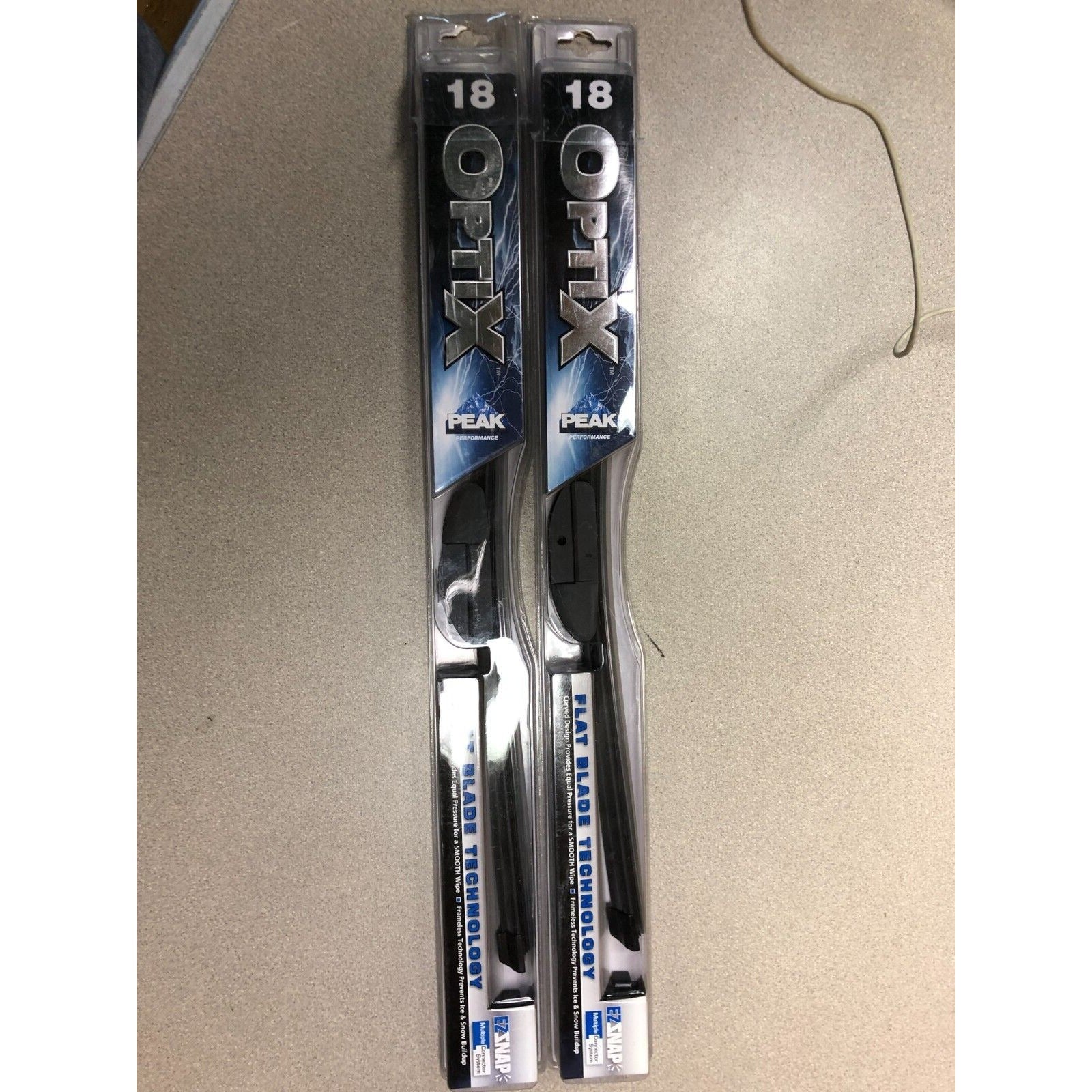 Two packages of Optix peak wiper blades on a beige surface