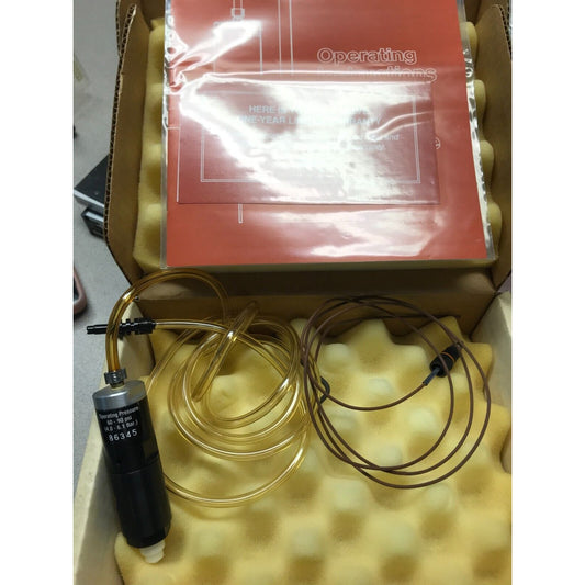 EFD Liquid Metering Valve 86345 placed in front of its packaging box with foam padding. The valve has a black body with a label and a brown tube attached to it.