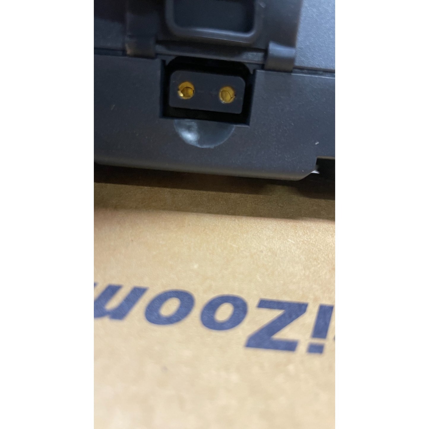 Close-up of a power adapter plug on a cardboard surface with 'Uooz!' branding.