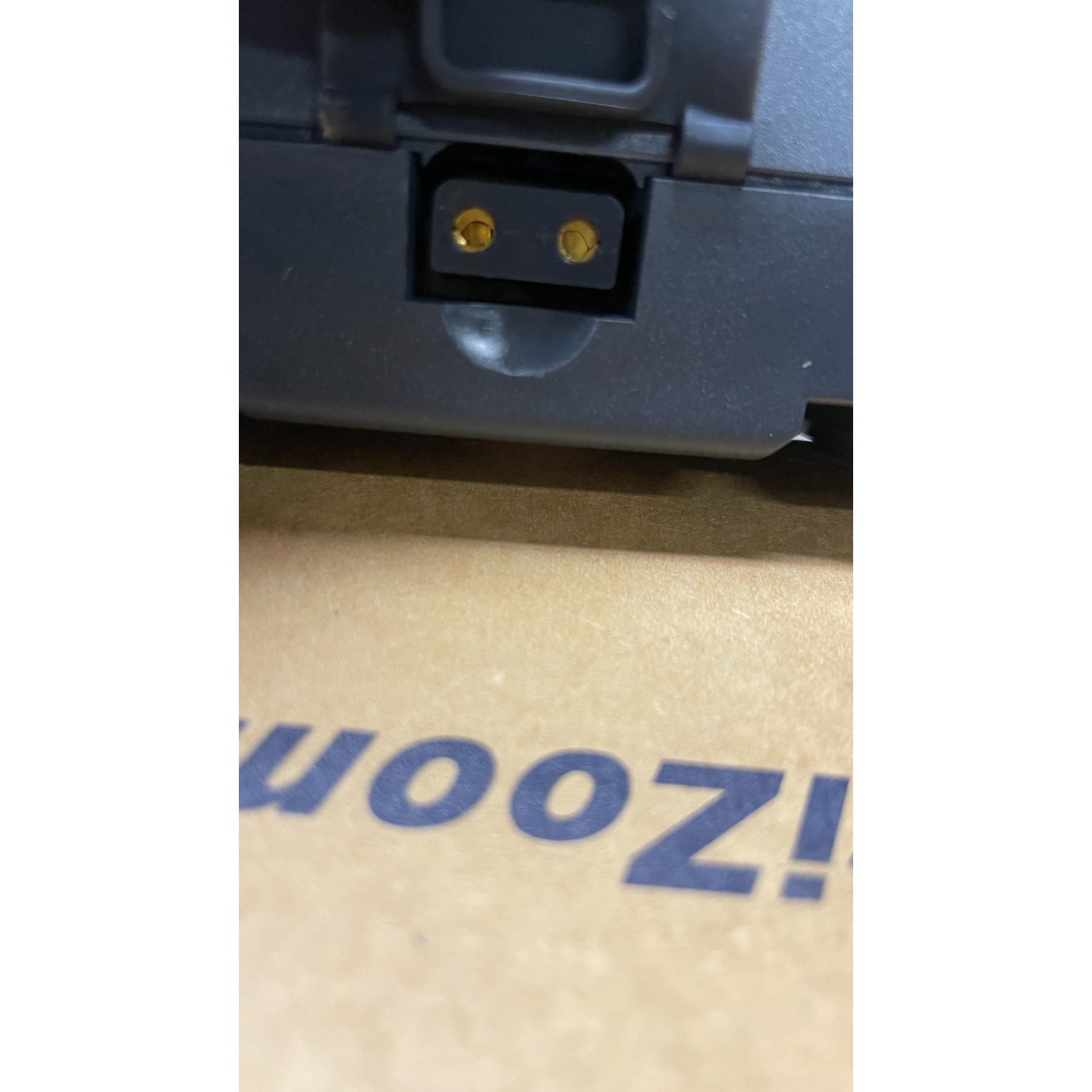 Close-up of a power adapter plug on a cardboard surface with 'Uooz!' branding.