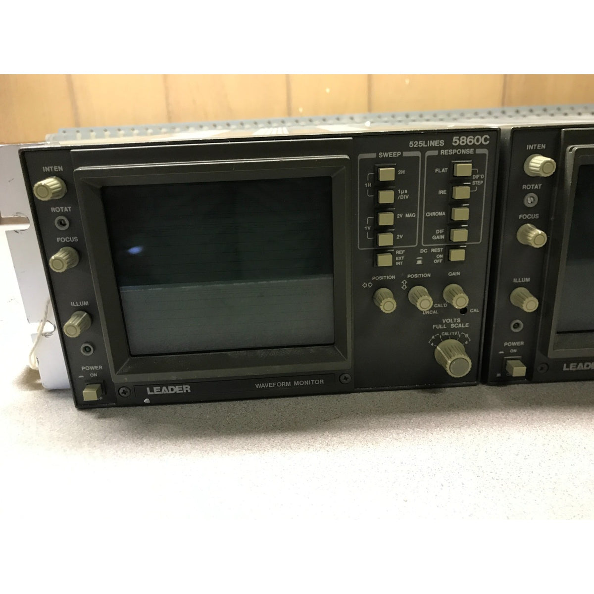 A LEADER 5980C 125-line waveform monitor display unit with a dark screen and multiple control knobs, photographed on a light surface with a wood background.