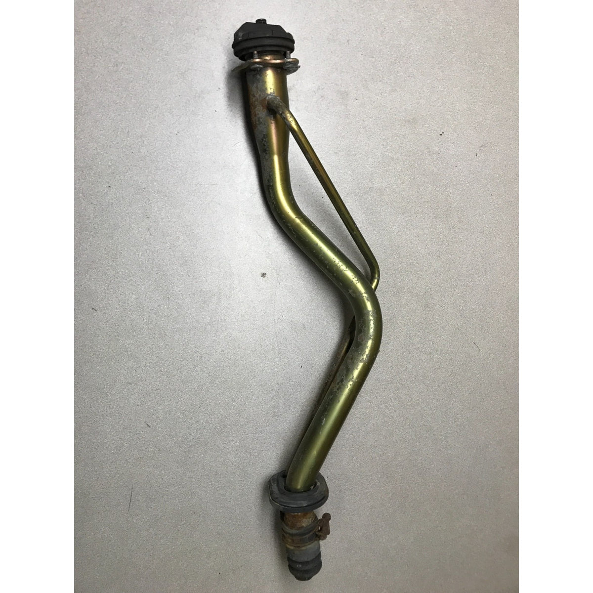 A used metal automotive part, likely a bracket or linkage arm, featuring a brass-colored body with black plastic or rubber end caps and mounting hardware, photographed on a neutral light gray background. 1993-1997 Honda Civic Del Sol OEM Gas Filler Neck