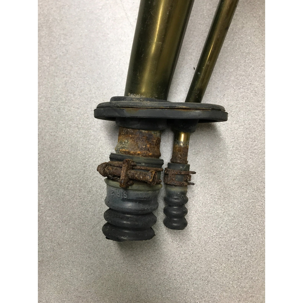 A close-up of a used industrial or automotive component featuring two brass-colored metal tubes, a black rubber gasket, and a rusted metal clamp assembly on a light gray background. 1993-1997 Honda Civic Del Sol OEM Gas Filler Neck