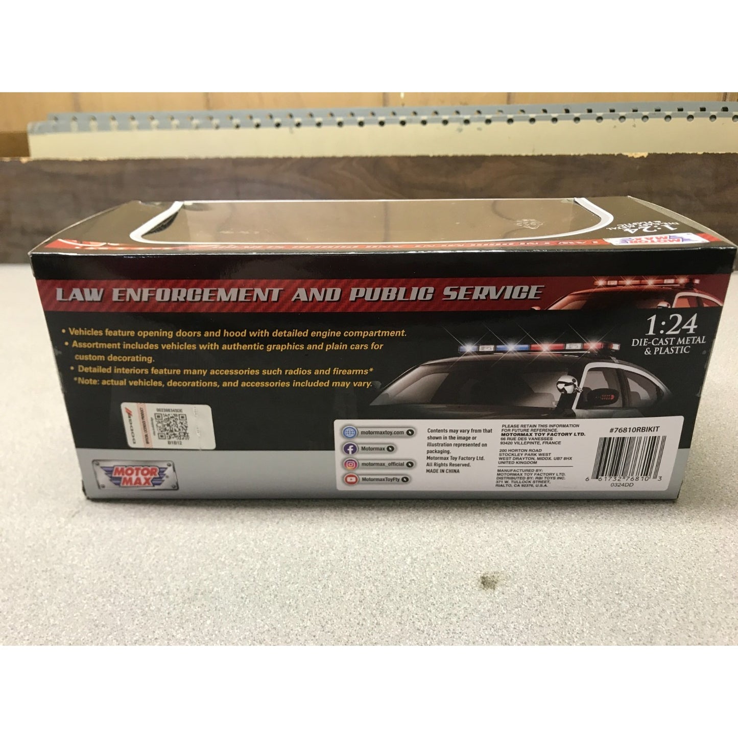 Box packaging for a 1:24 scale toy car, shown from the back side. The box is black with red and white text, featuring an image of a police car with flashing lights and the title 'LAW ENFORCEMENT AND PUBLIC SERVICE'.