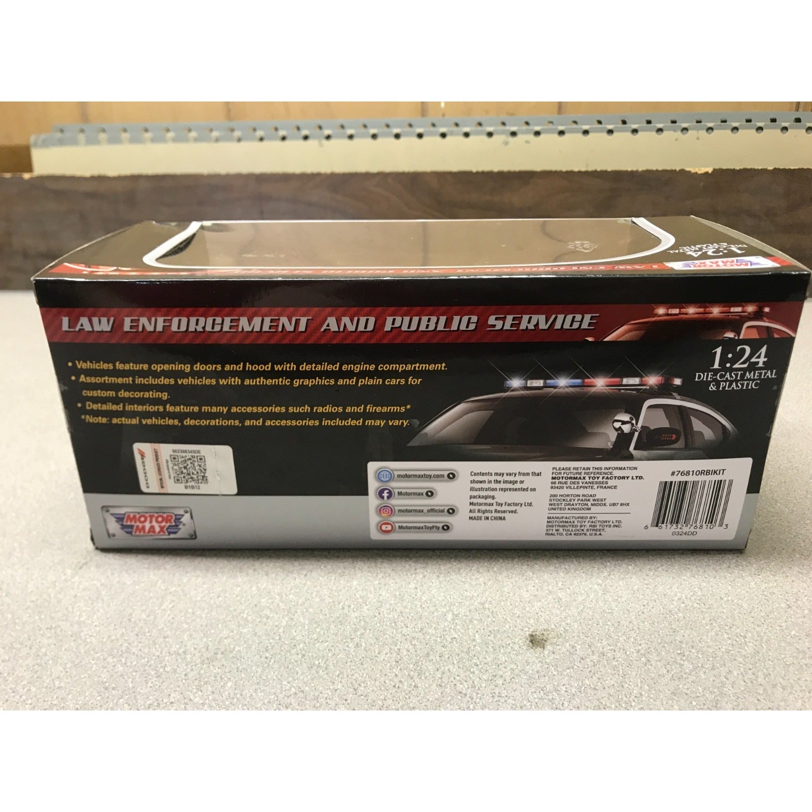 Box packaging for a 1:24 scale toy car, shown from the back side. The box is black with red and white text, featuring an image of a police car with flashing lights and the title 'LAW ENFORCEMENT AND PUBLIC SERVICE'.
