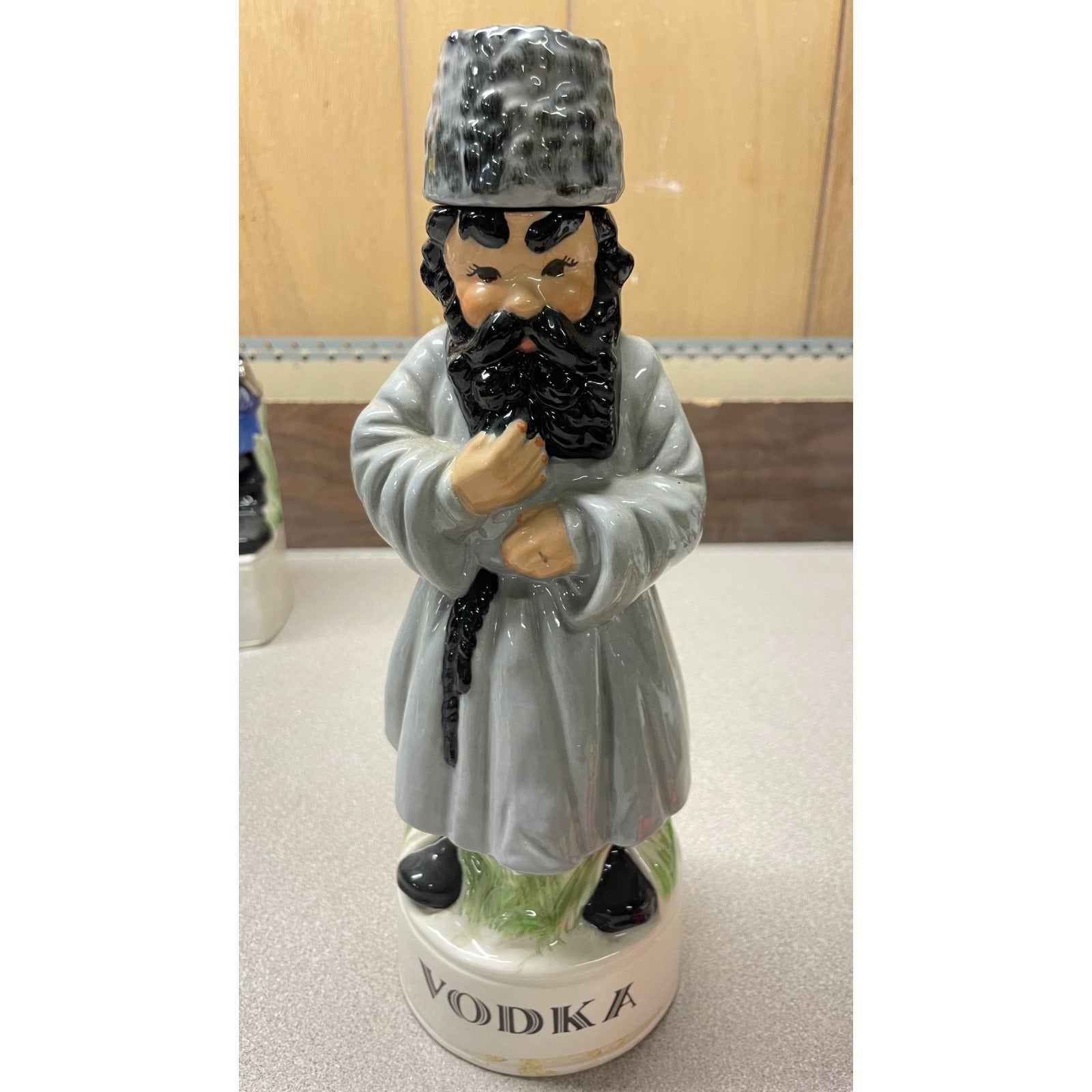 Statue of a man in traditional attire on a vodka bottle with a wooden background