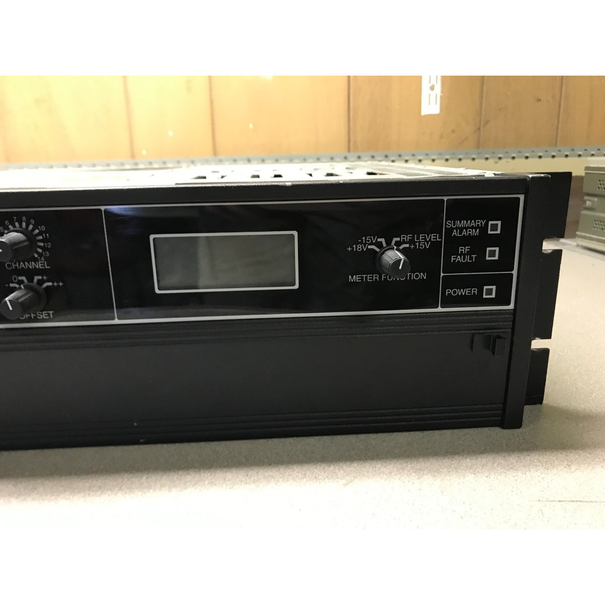 A black rack-mount electronic device with a front control panel, featuring a small display screen, rotary knobs, and labeled switches including CHANNEL, METER FUNCTION, RF FAULT, SUMMARY ALARM, and POWER.