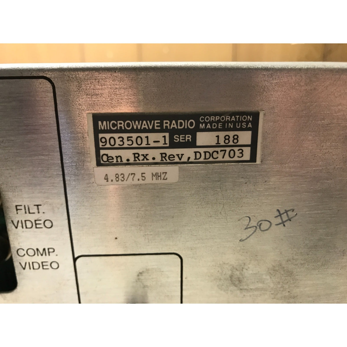 Close-up of a silver metal microwave radio chassis with a black and white manufacturer label reading 'MICROWAVE RADIO CORPORATION MADE IN USA' and handwritten markings.