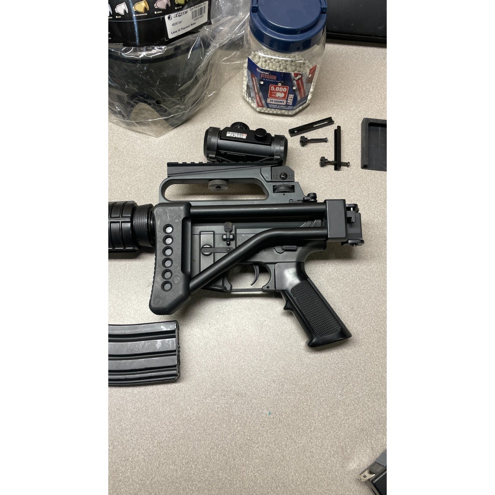 DPMS Panther Arms U050810381 M4 Style Airsoft Gun Lot UNTESTED, Accessories and Bag Included. Swiss Arms Sight, DYE i4 Goggle Lens, Crosman .20 Grams Airsoft closeup of side of gun with accessories in background