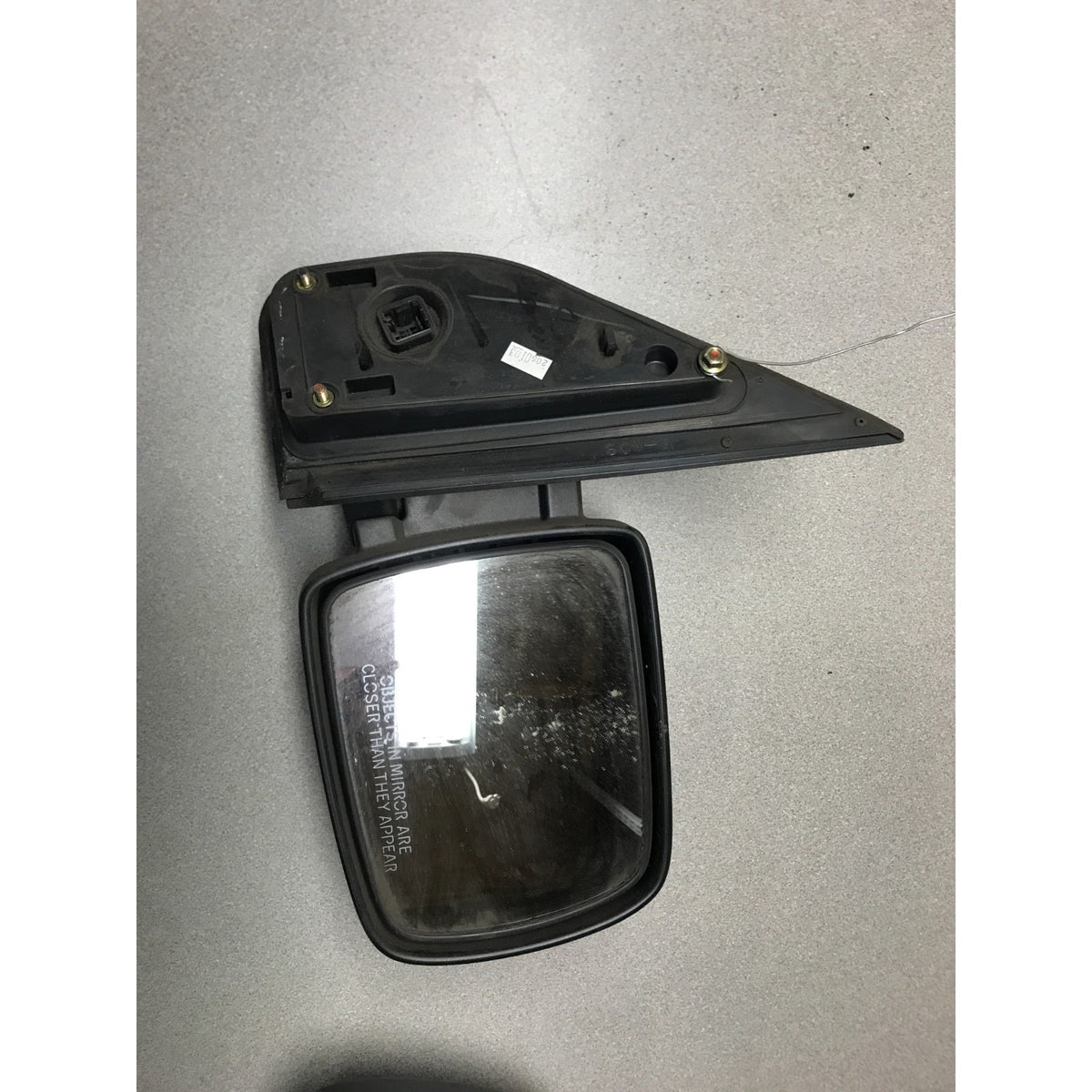 A used black side-view mirror assembly with a clear glass mirror and mounting bracket, photographed on a gray concrete floor. 2003-2008 Honda Element Side View Mirrors - Driver and Passenger Side