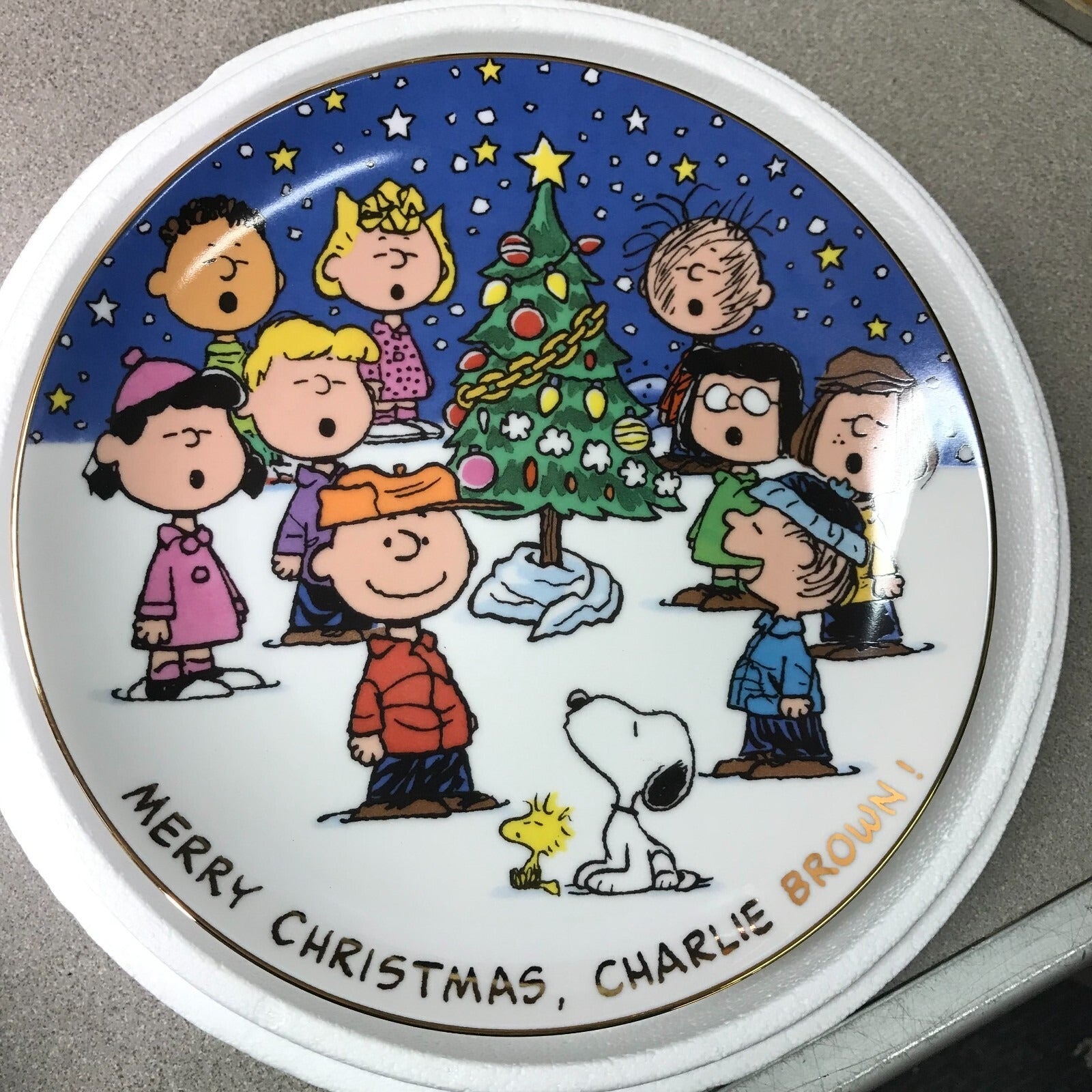 Circular plate with Christmas-themed illustration of Charlie Brown and friends around a tree, with 'Merry Christmas, Charlie Brown!' text.