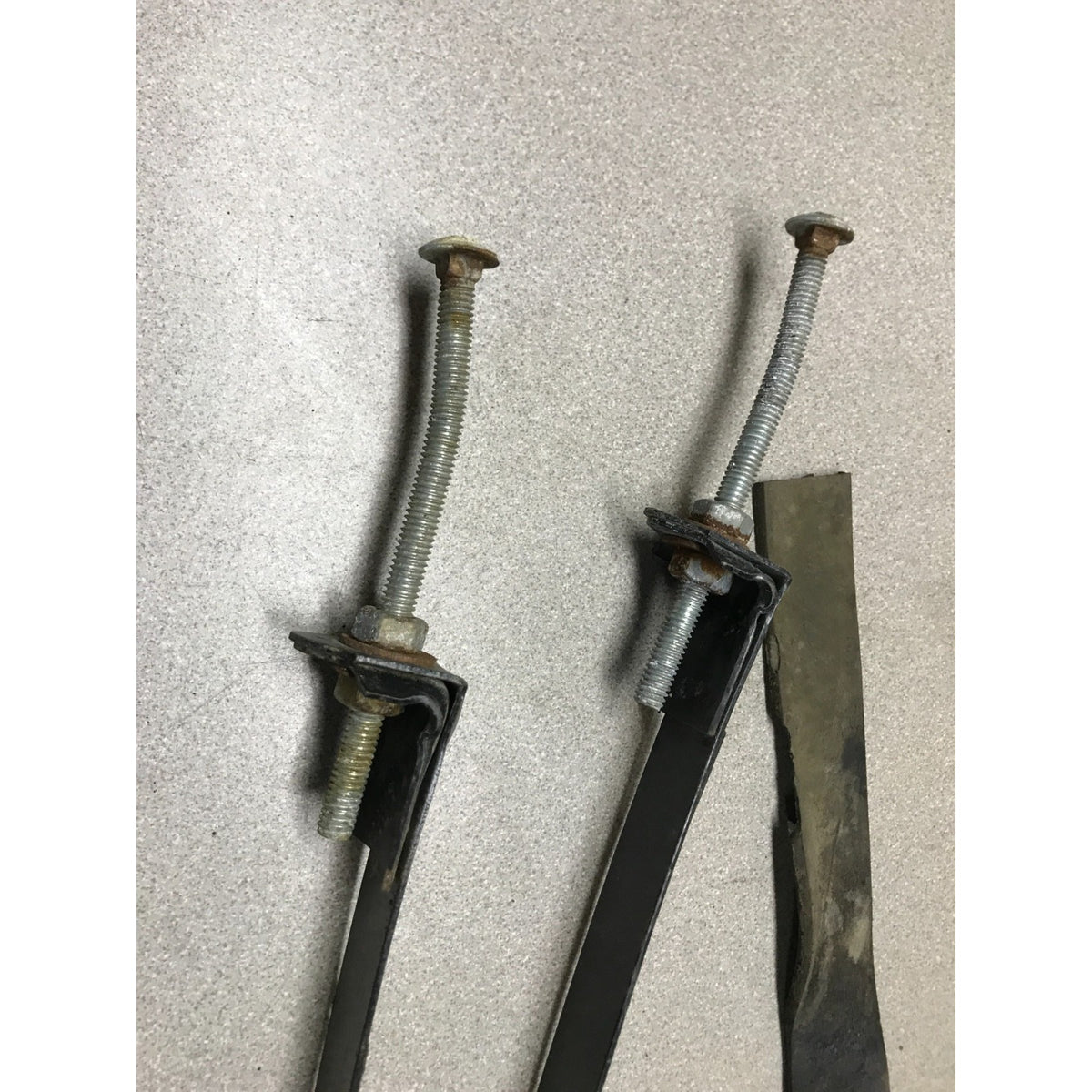 Two long black metal bars with threaded bolt assemblies and a dark metal blade, photographed on a light speckled surface. 1993-1997 Honda Civic Del Sol Gas Tank Straps Set close up of bolts slightly bent