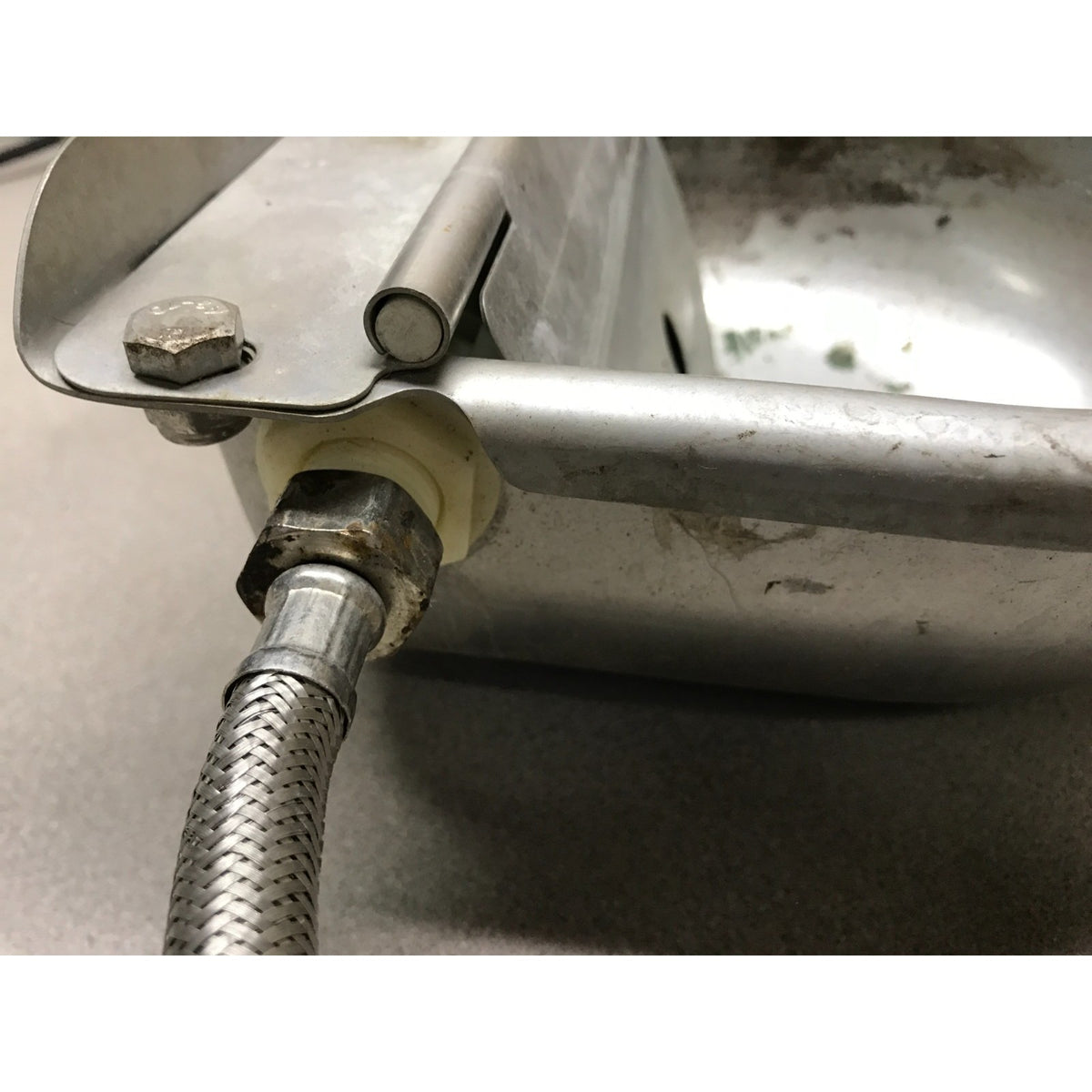 Close-up of a stainless steel sink faucet assembly with a braided metal water supply hose connected, set against a gray sink background.