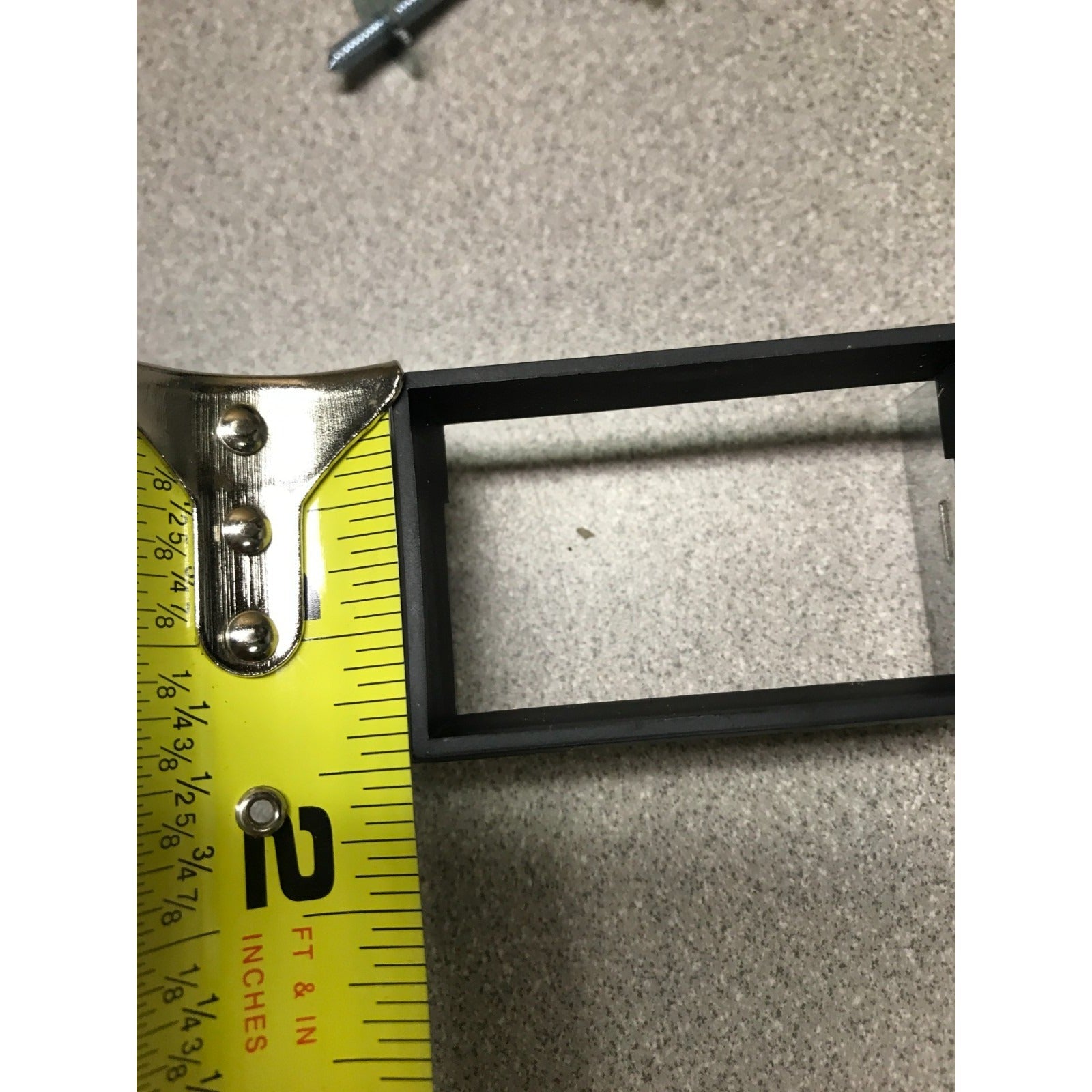 Black picture frame with a measuring tape showing dimensions on a gray surface