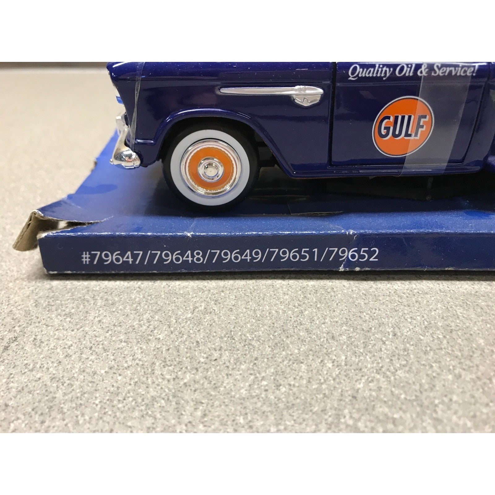 A blue vintage Gulf Oil truck model or miniature displayed on its blue base box, with the Gulf logo visible on the side and a gray textured surface in the background.