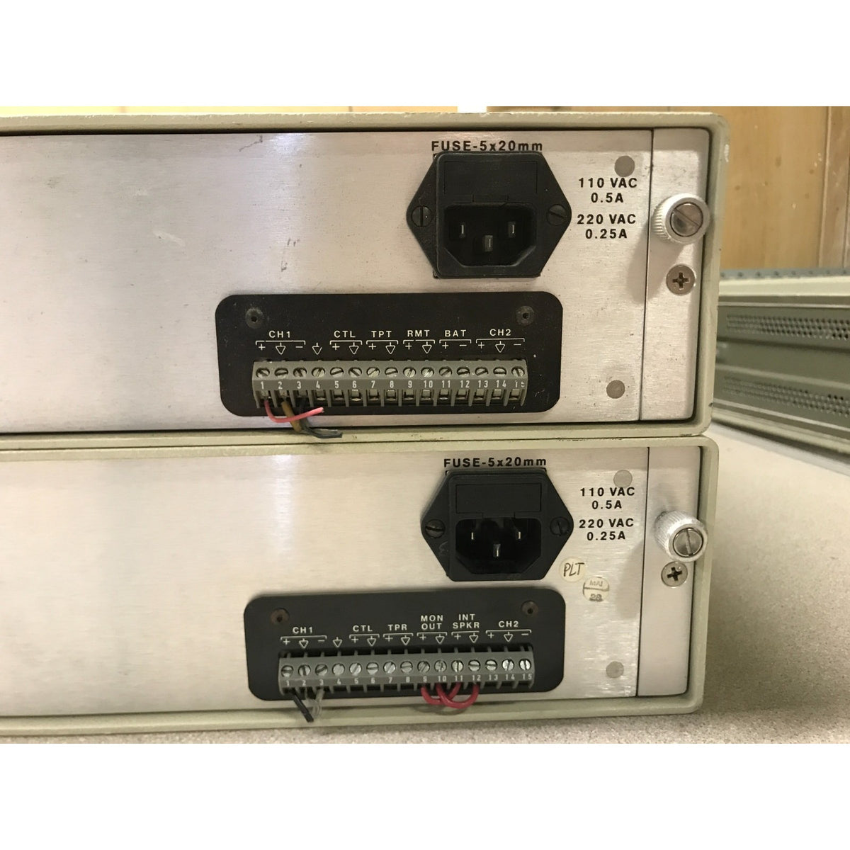Two stacked industrial electronic power supplies with metal front panels, terminal blocks, fuses, and AC input connectors on a light surface. Moseley CL-100 Communications Link back panel closeup