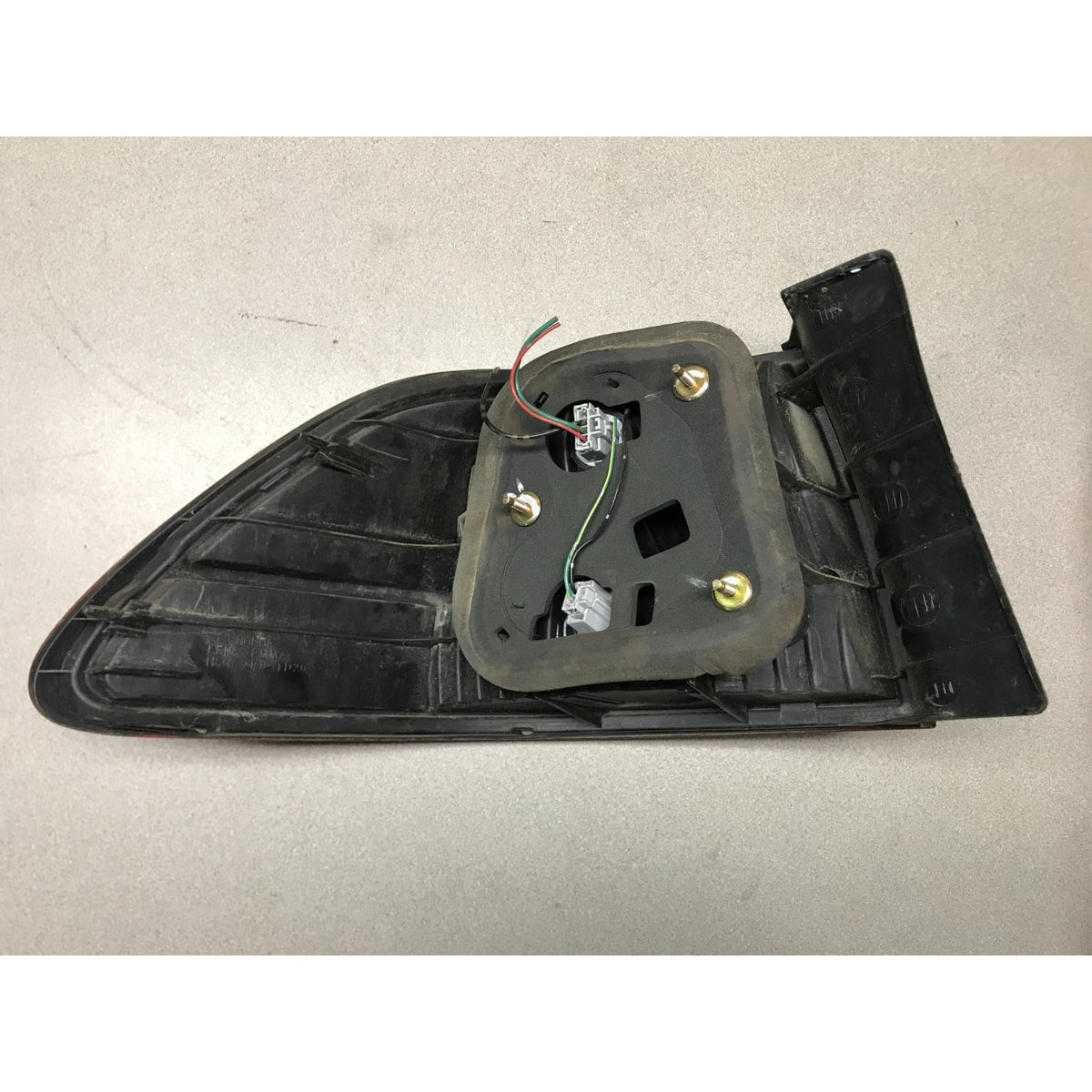 A black plastic automotive light assembly, likely a tail light or side marker, with its internal mounting bracket, screws, and wiring harness exposed, photographed on a neutral gray surface. 2001-2002 Honda Accord Sedan OEM Tail Lights - Full Set back view
