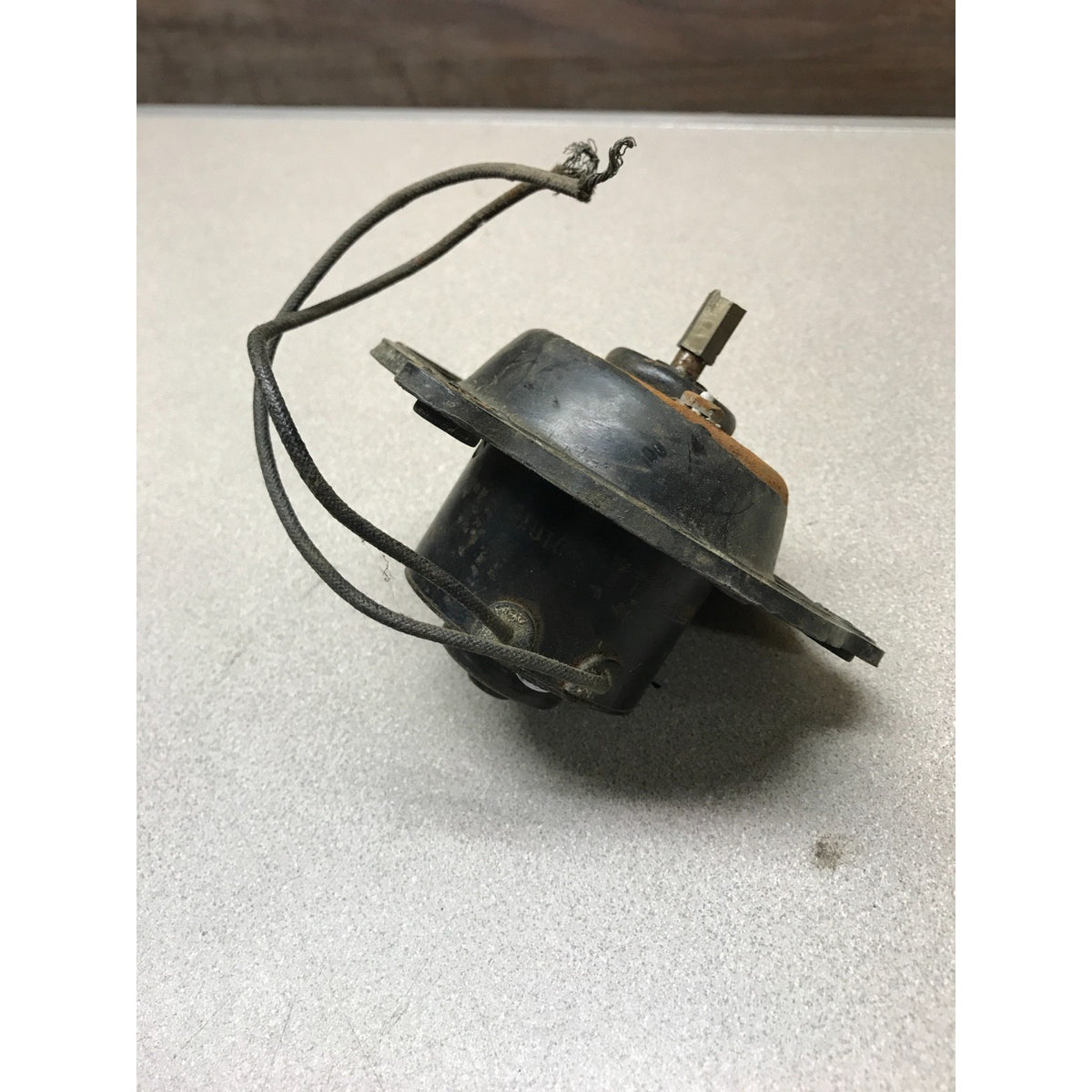 
Auto-Lite EMY-4002 Defroster Motor with BracketA used black plastic electrical component with attached wires and a metal terminal, photographed on a light gray surface.