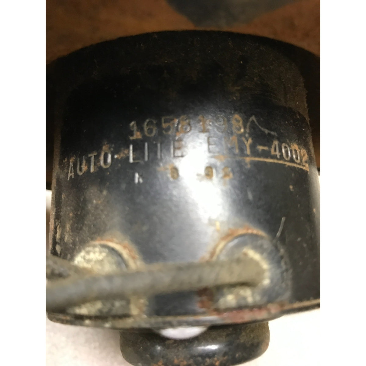 A close-up of a used black automotive capacitor with stamped text reading 'AUTO-LITE EMY-4002' and '1656198A'.