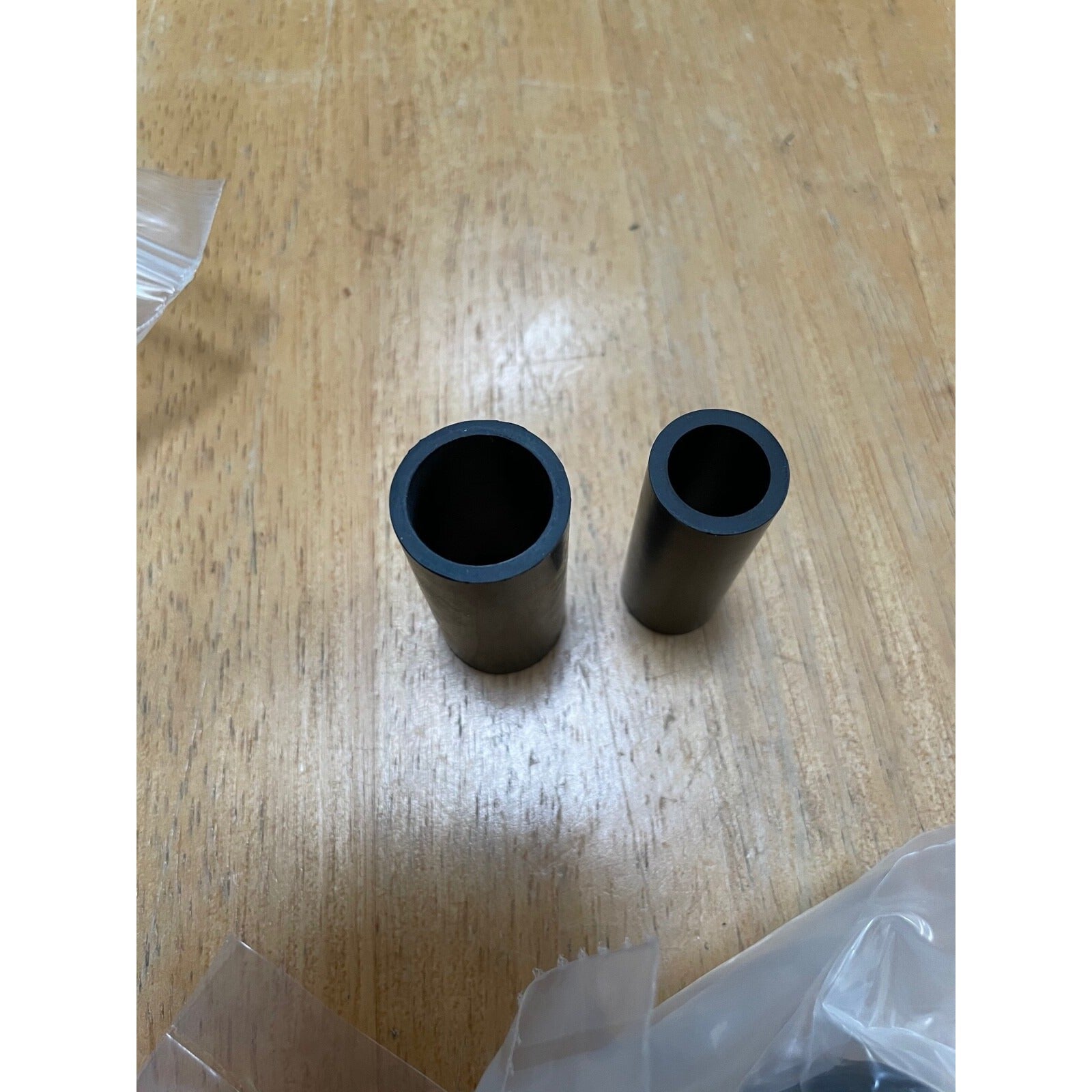 Two black cylindrical objects on a wooden surface with plastic wrap.
