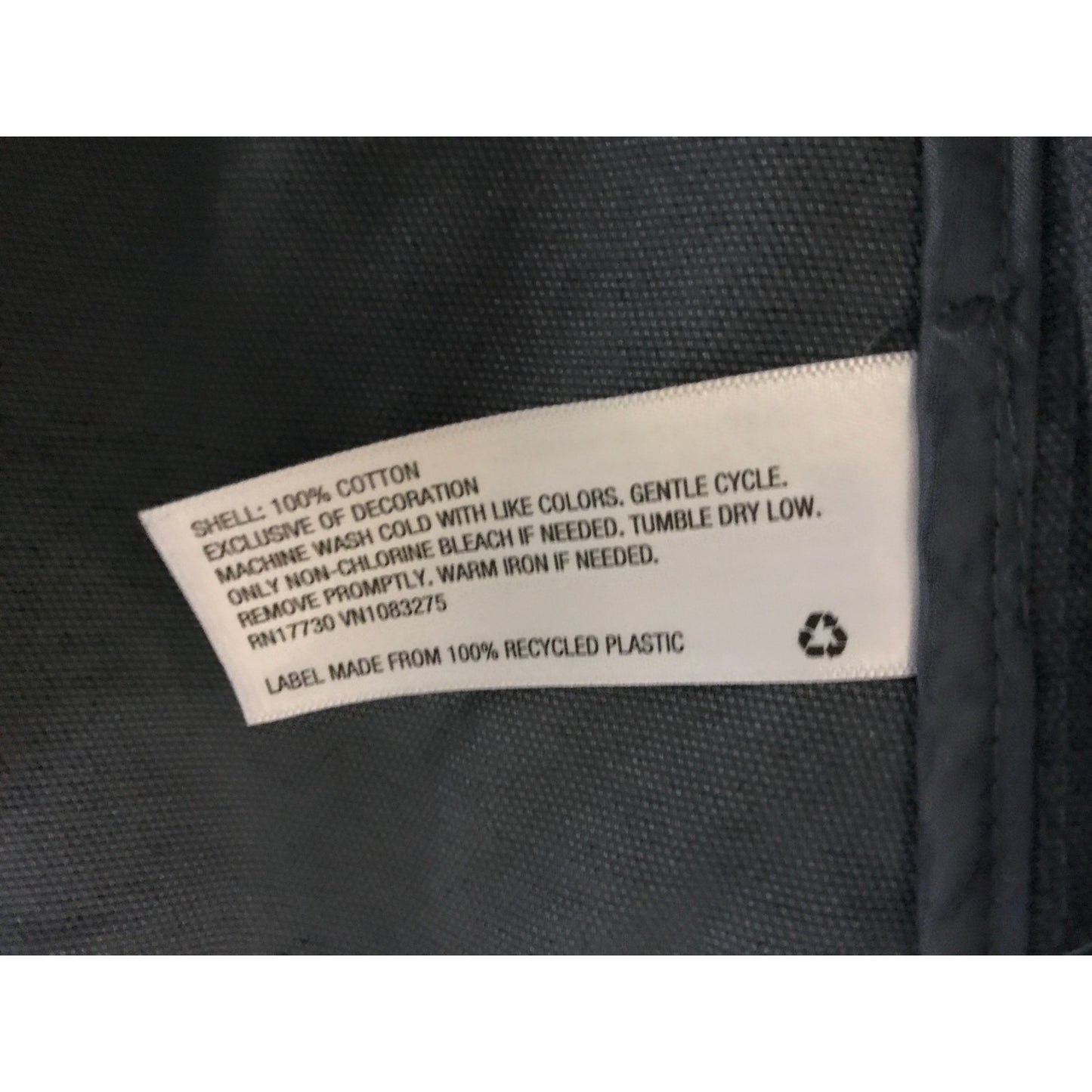 Clothing label on a black fabric background with washing instructions and material information.