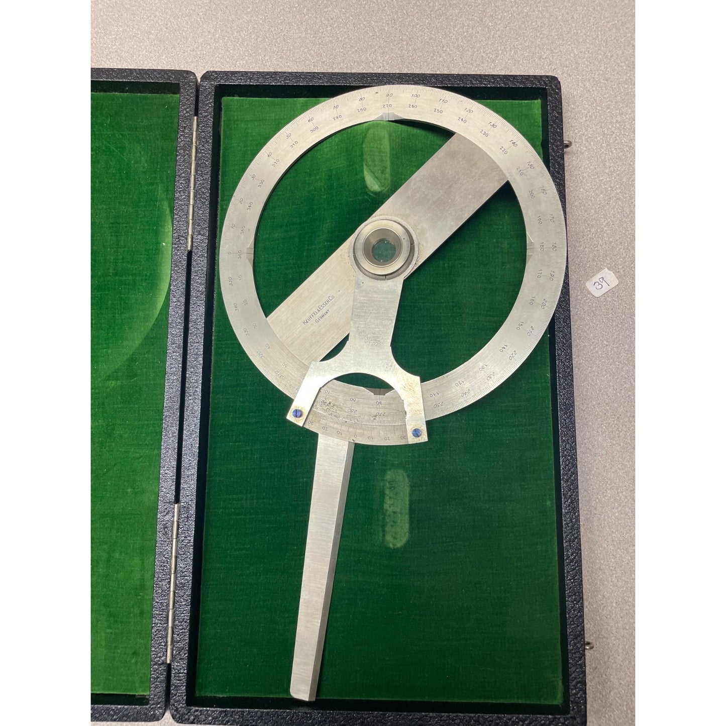 A vintage metal surveyor's square or angle measuring tool with engraved markings, displayed inside an open black case lined with green velvet. Keuffel &amp; Esser Co. 1221 1/2 8 Inch Protractor Drafting Tool with Case, Made in Germany
