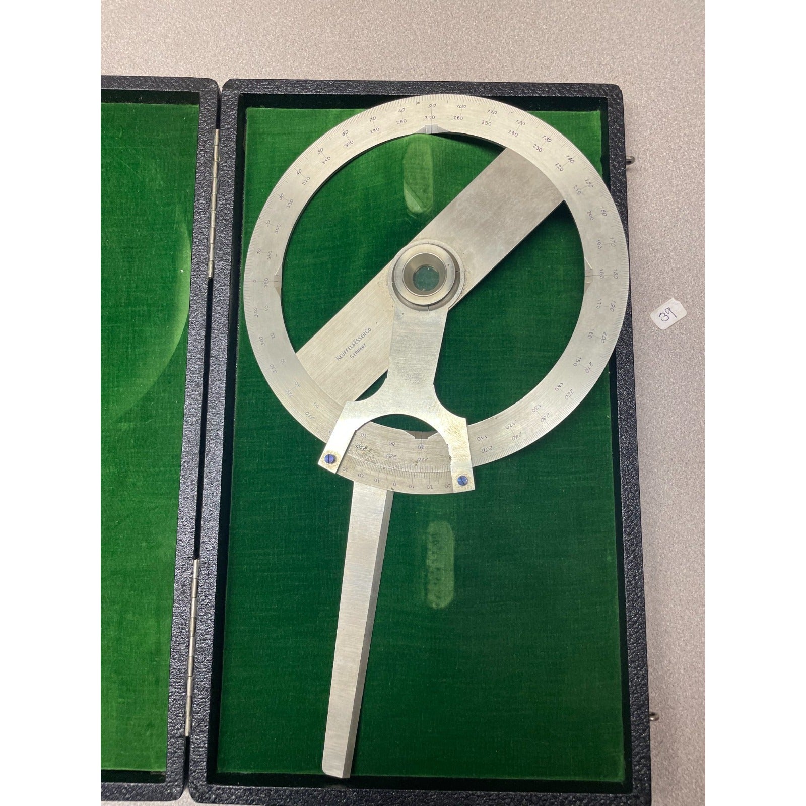 A vintage metal surveyor's square or angle measuring tool with engraved markings, displayed inside an open black case lined with green velvet. Keuffel &amp; Esser Co. 1221 1/2 8 Inch Protractor Drafting Tool with Case, Made in Germany