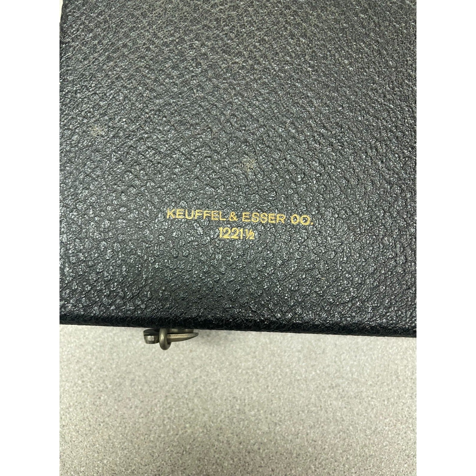 Close-up of a textured black leather case with gold foil embossed branding reading 'KEUFFEL & ESSEN DO. 12013' on a light gray background.