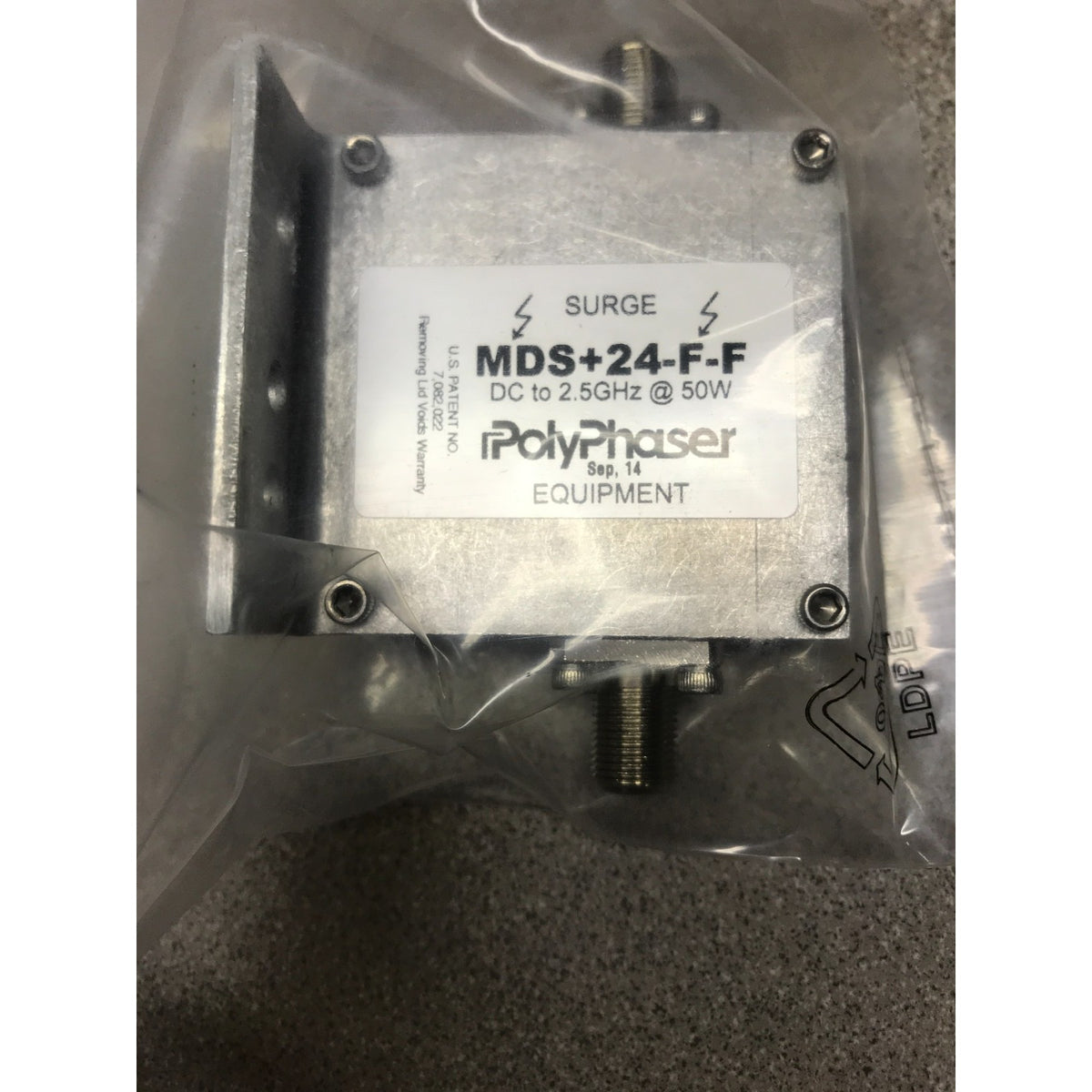 A PolyPhaser MDS+24-F-F surge protector for telecom equipment, sealed in a clear plastic bag. The device is made of silver metal with a white label showing the PolyPhaser brand and model details.
