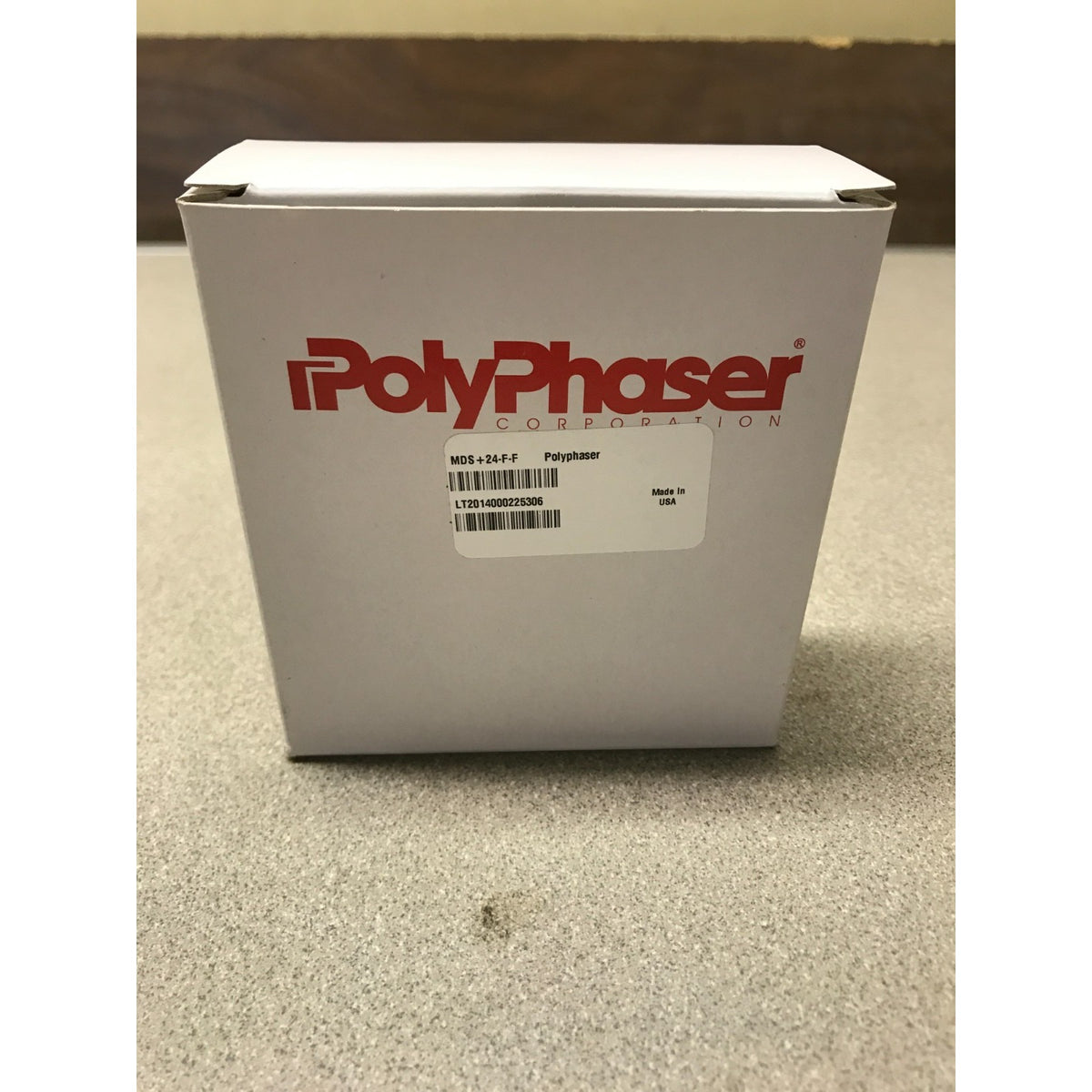 A white PolyPhaser Collection product box with red branding and a barcode label, standing on a textured gray floor.