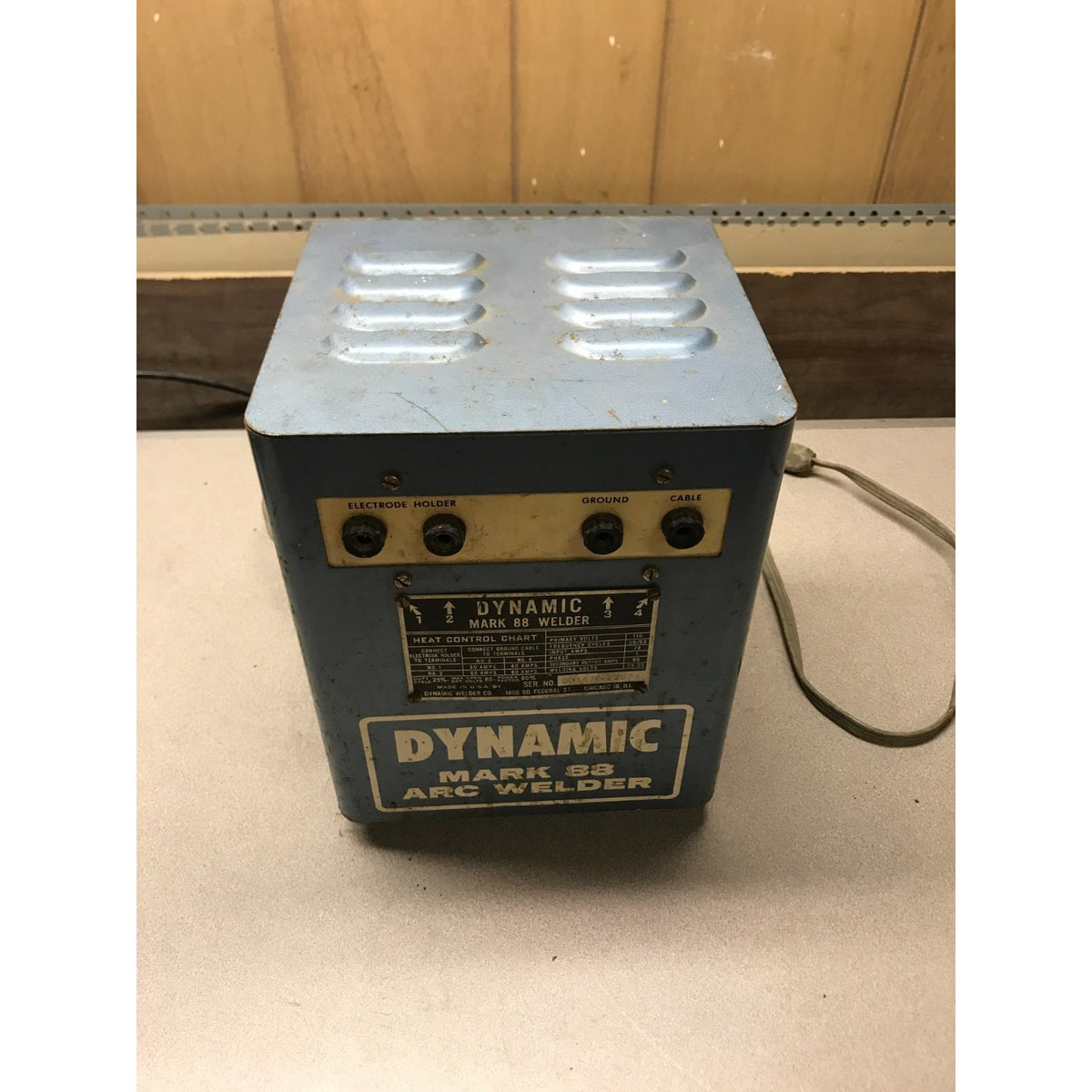 A vintage Dynamic Mark 52 Arc Welder machine with a blue-gray metal body, gold-colored control panel, and black dials, sitting on a light-colored surface.