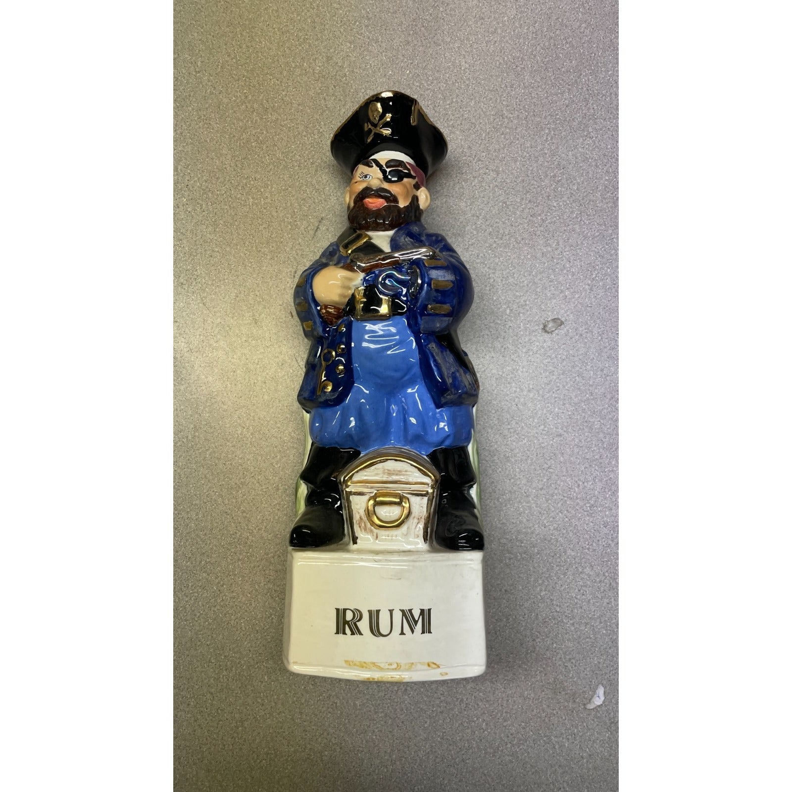 Figurine of a person in blue uniform holding a bottle labeled 'Rum' on a gray background