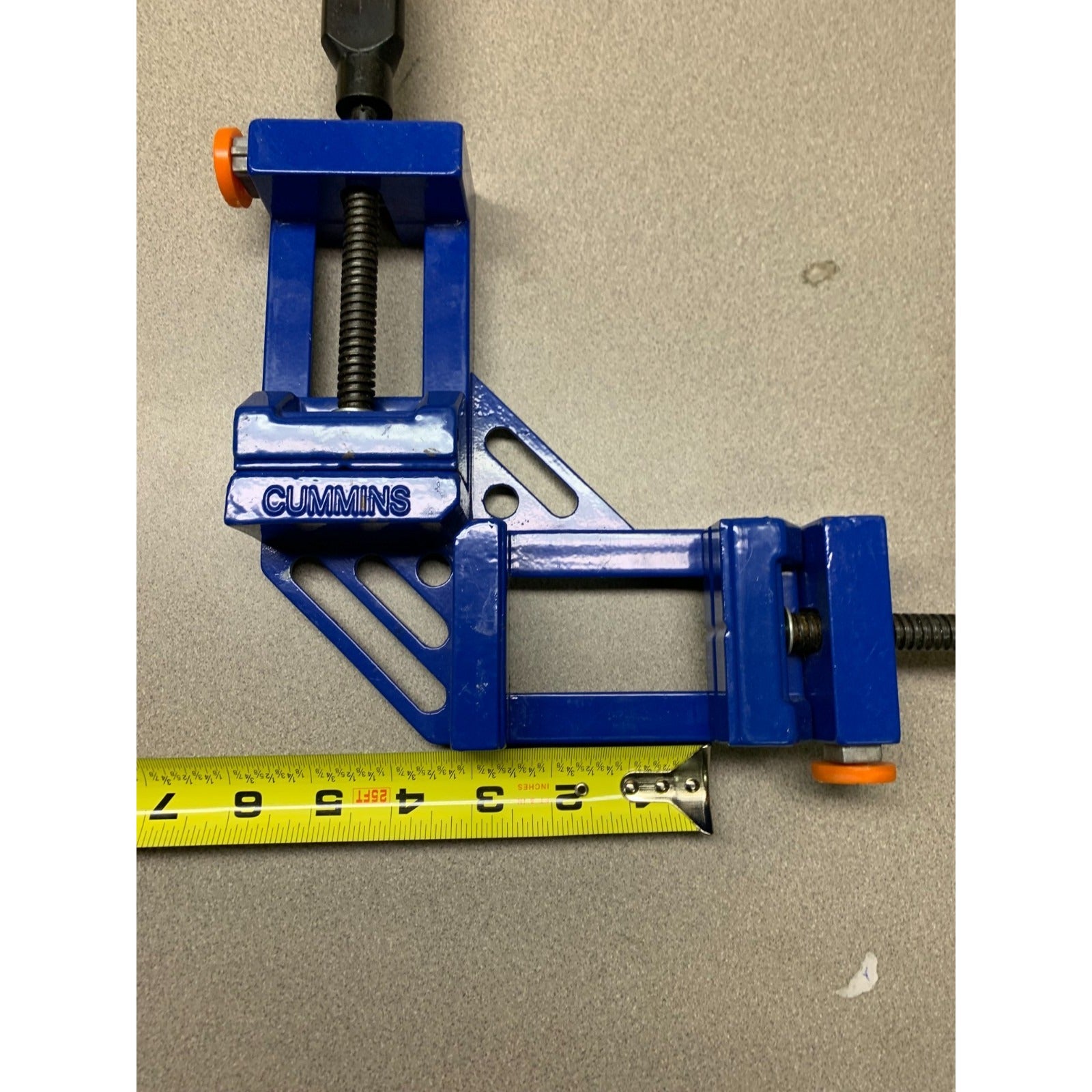 Blue vise with 'Cummins' branding on a beige background with measuring tape indicating size